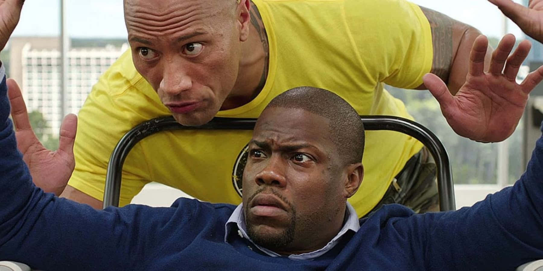 comedy 桌布 壁紙 — 巨石強森在緊張的喜劇時刻俯身靠近凱文·哈特，雙手舉起，背景是城市天際線。