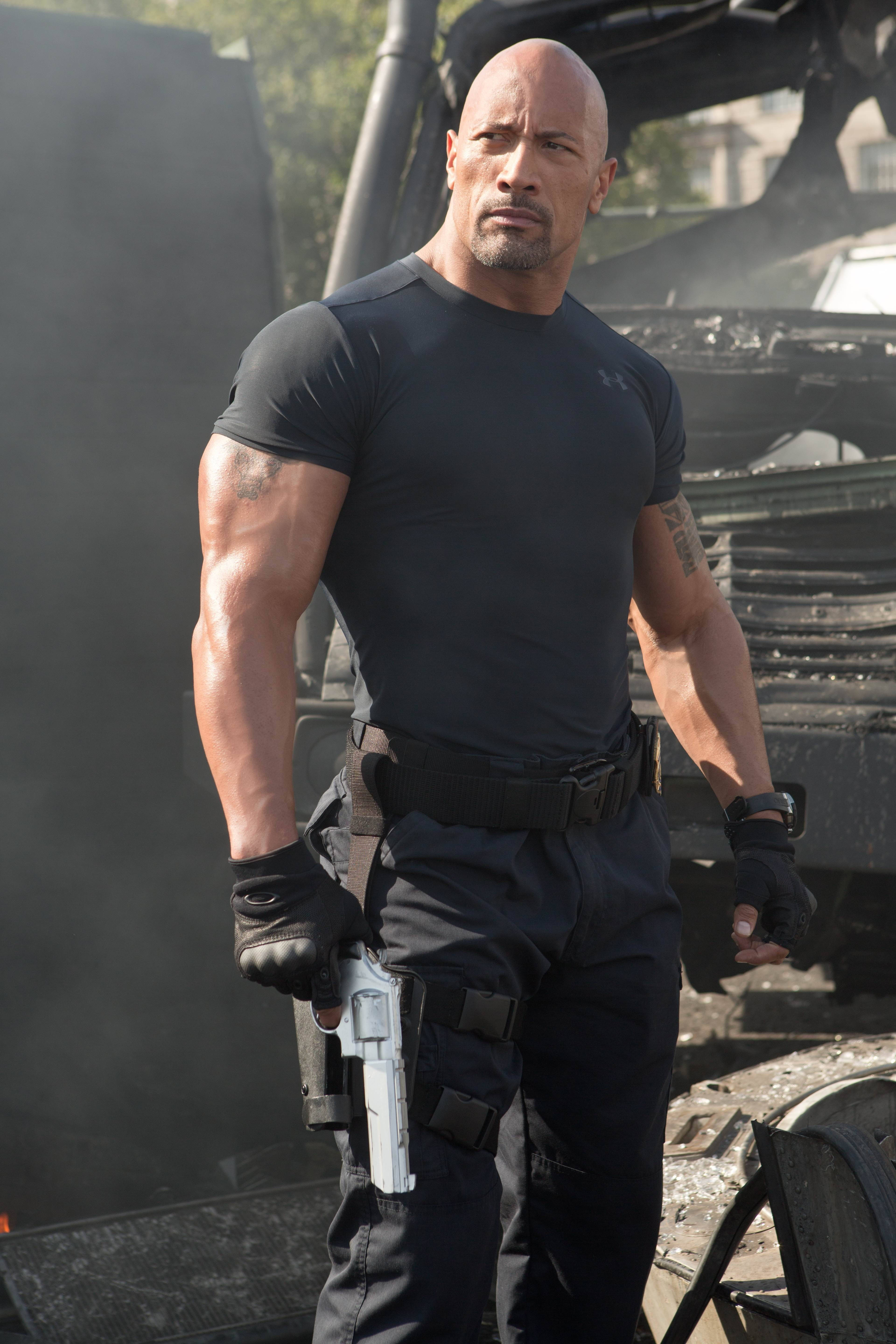 Dwayne 桌布 壁紙 — 巨石強森肌肉發達、神情專注，身穿黑色戰術服裝，在煙霧和廢墟中手持手槍。