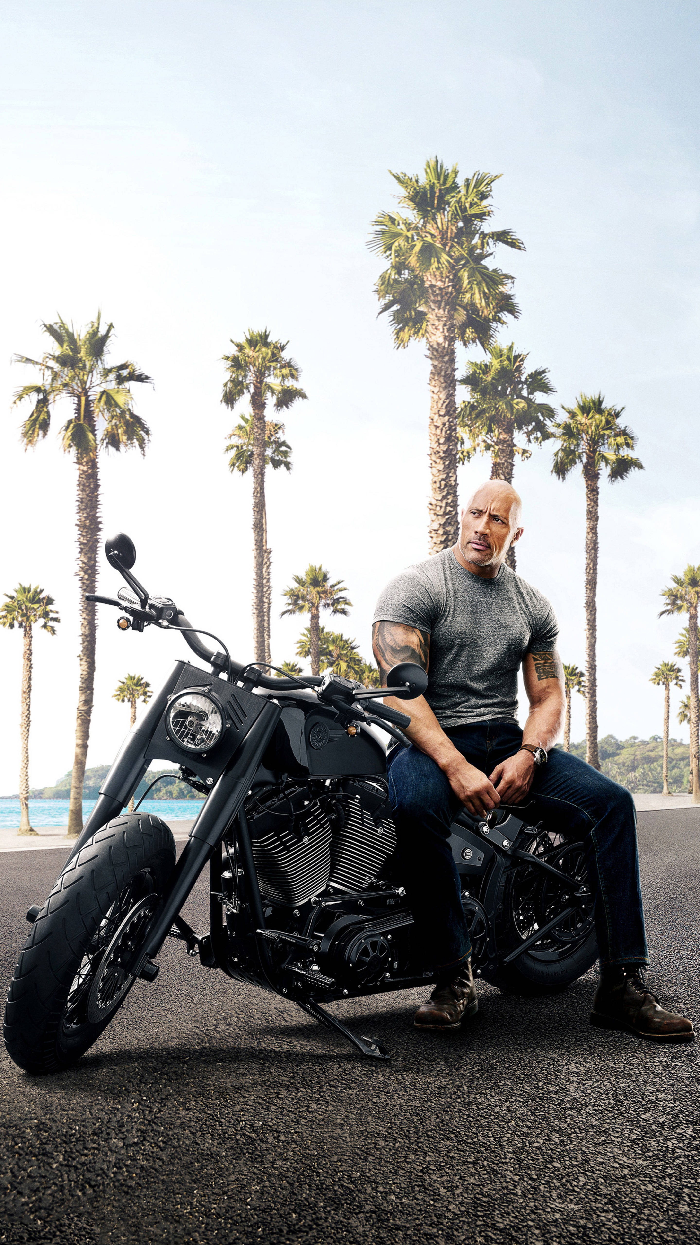 Dwayne 桌布 壁紙 — 巨石強森自信地坐在一輛黑色chopper機車上，背景是高聳的棕櫚樹和明亮的藍天。