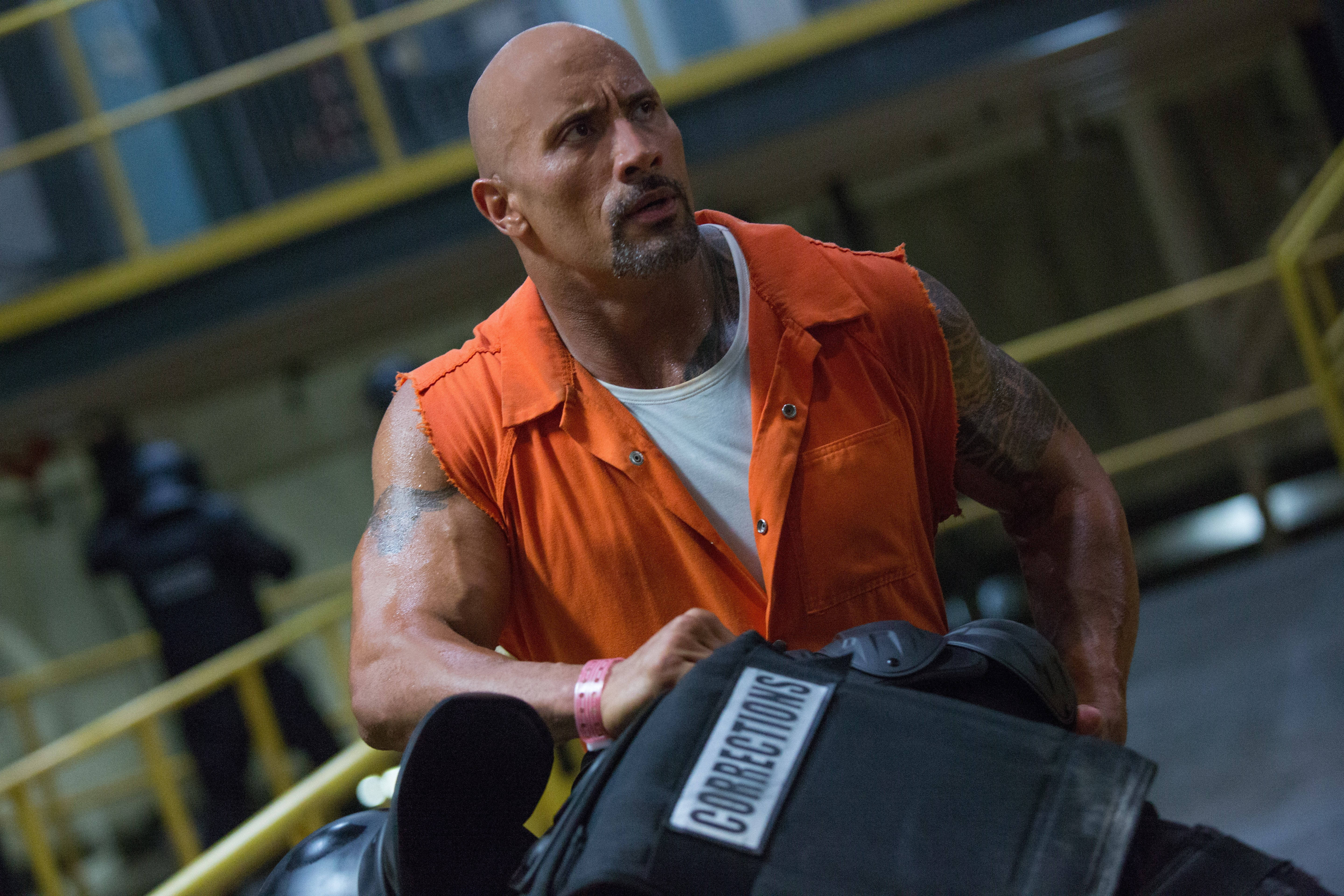 The Rock 桌布 壁紙 — 巨石強森身穿橙色監獄連身衣，在緊張的工業環境中抓住矯正官的背心。