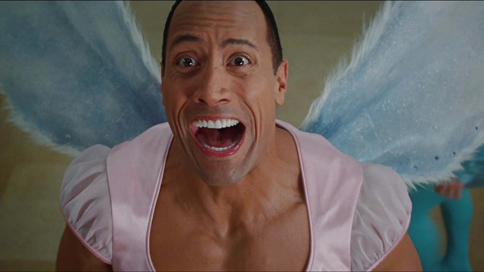 Tooth Fairy 桌布 壁紙 — 巨石強森飾演仙女，睜大眼睛，張開嘴巴，身穿粉紅色上衣和藍色翅膀。