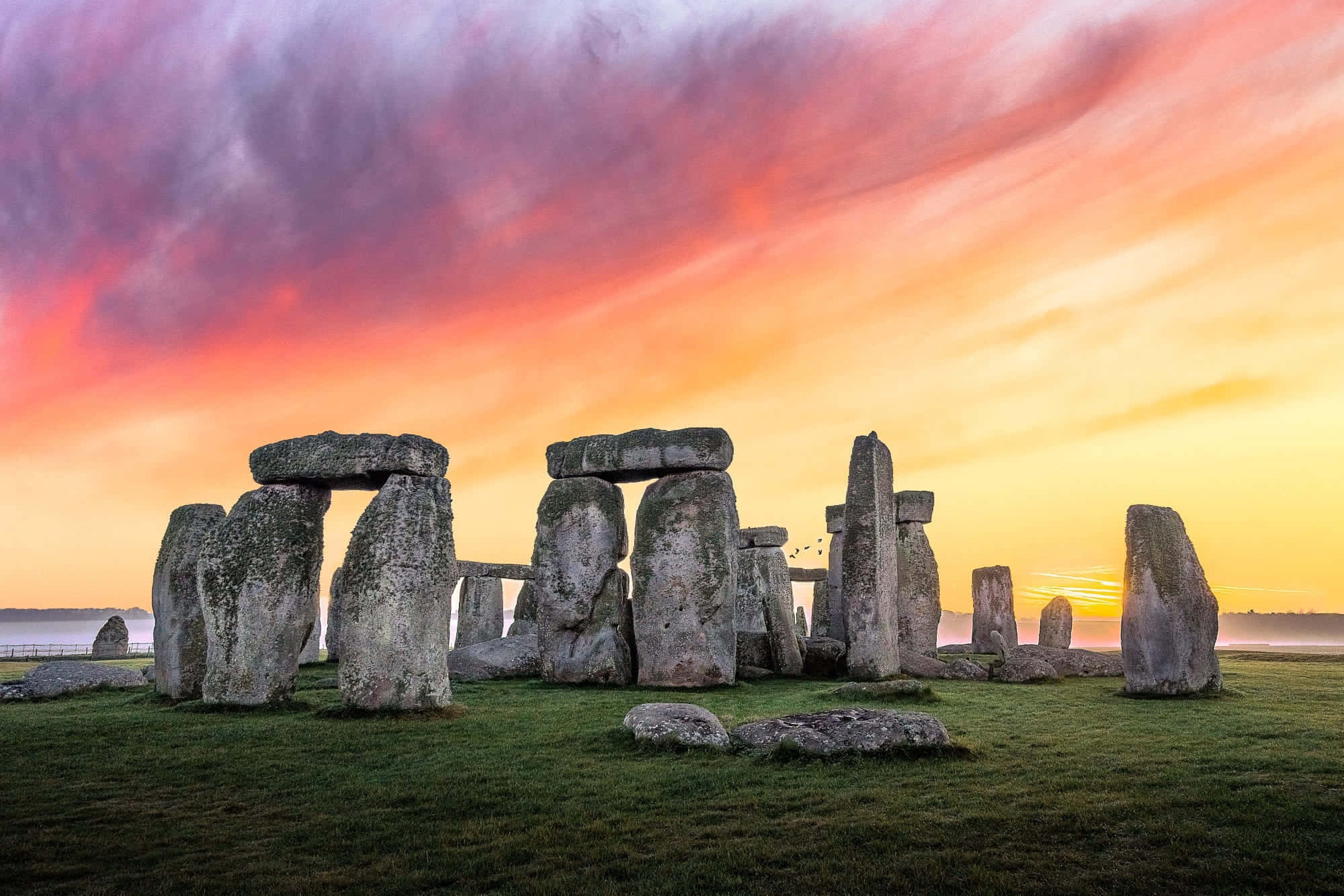 England 桌布 壁紙 — 巨石陣的古老立石在火紅的夕陽天空下雄偉地聳立，天空塗滿了橙色、粉紅色和紫色的條紋。