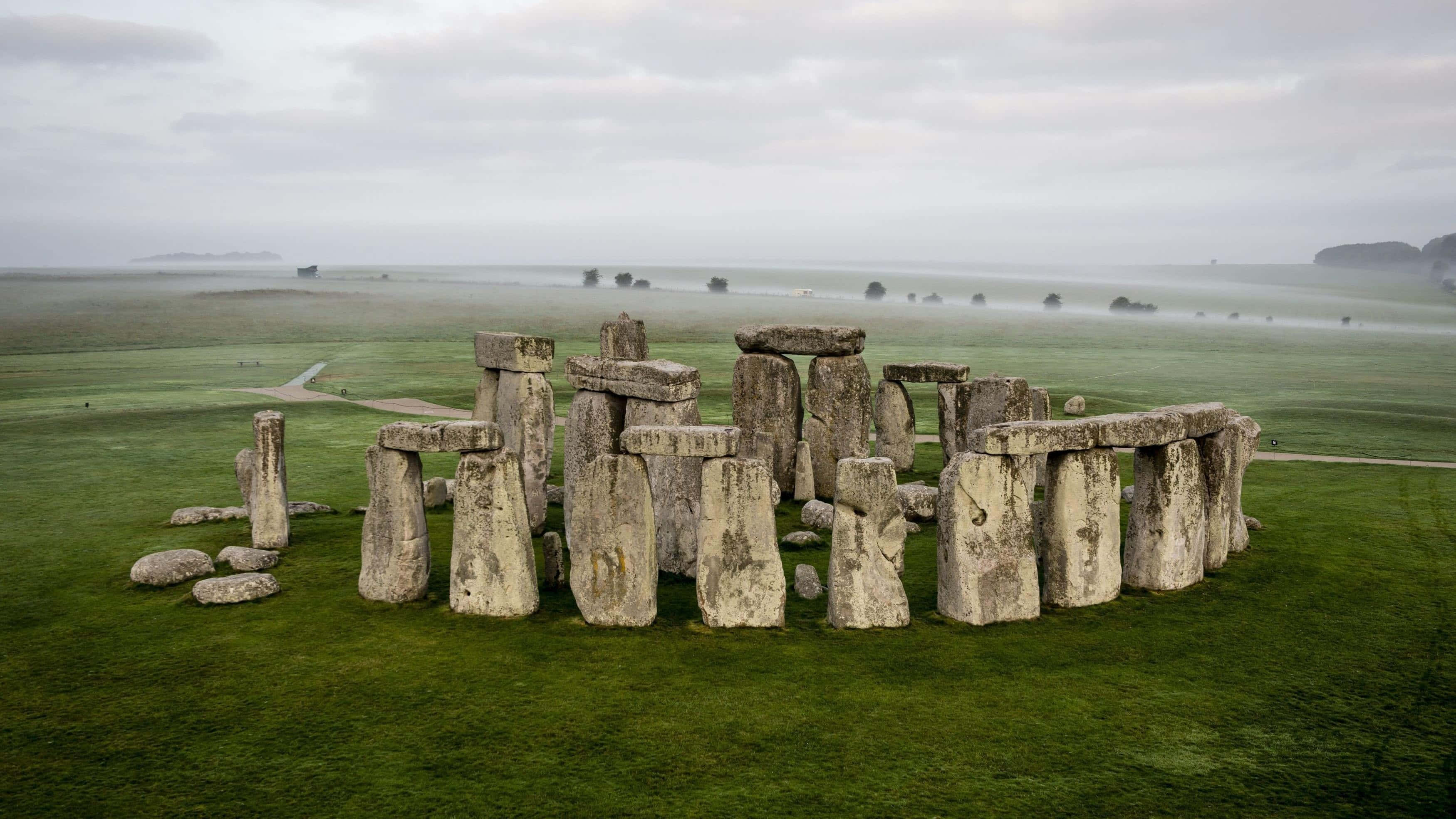 England 桌布 壁紙 — 巨石陣的古老立石在陰天之下，從霧氣瀰漫的綠色田野中莊嚴地聳立。