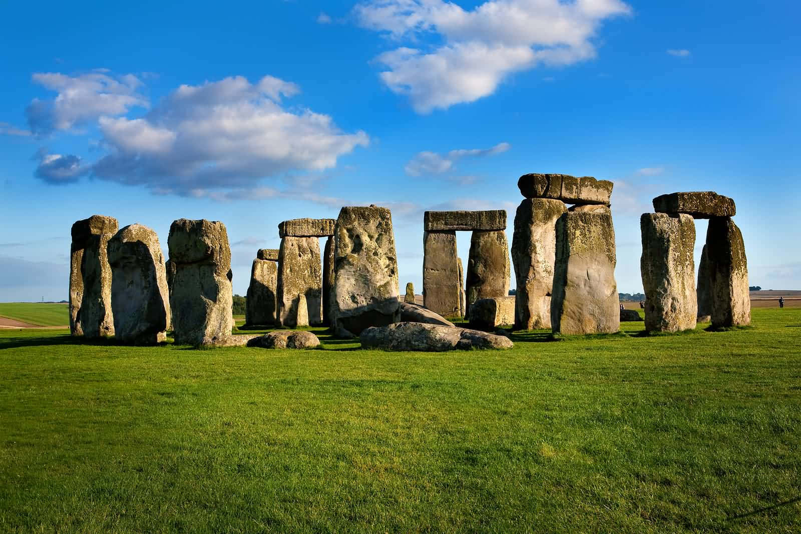 England 桌布 壁紙 — 巨石陣的古老立石從翠綠的草地上雄偉地升起，在明亮的藍天下散佈著白雲。