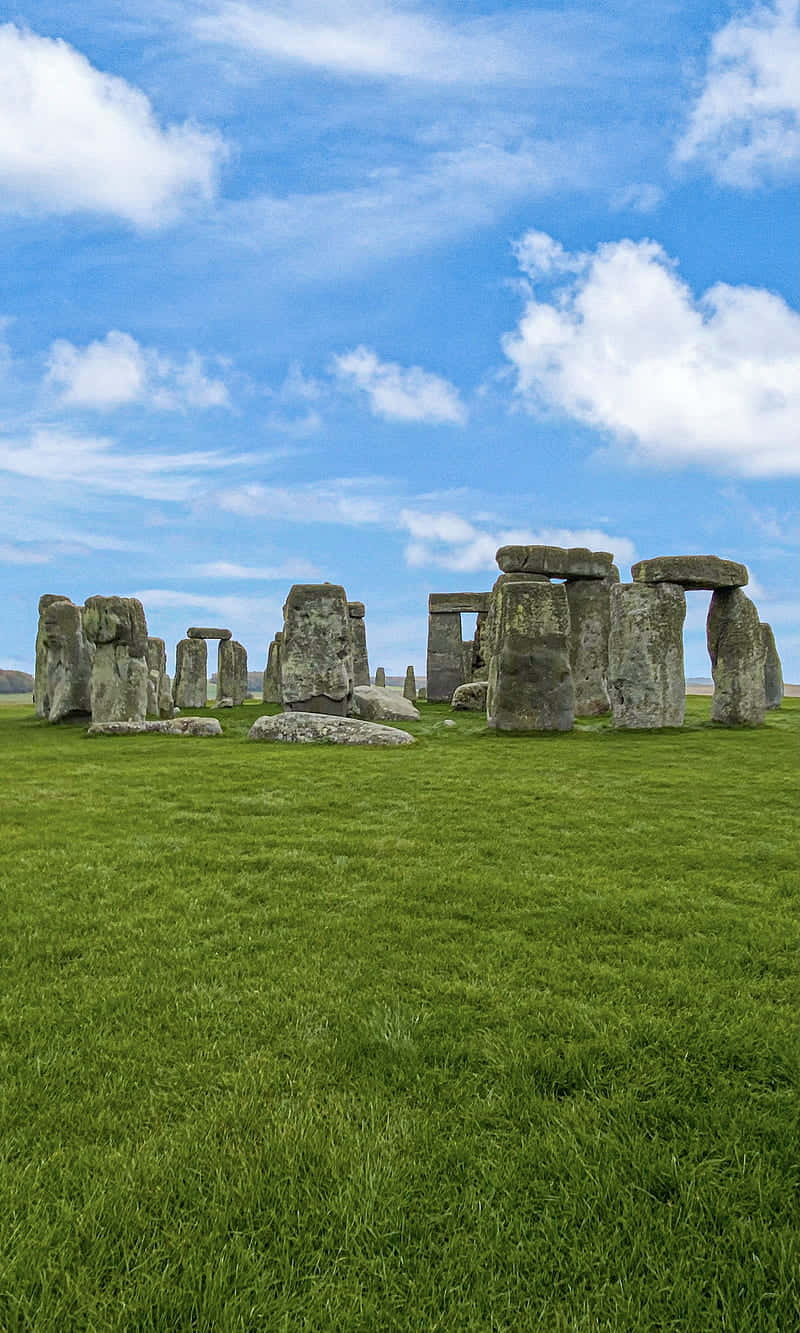 England 桌布 壁紙 — 巨石陣的古老立石從翠綠的草地上雄偉地升起，在明亮的藍天下有蓬鬆的白雲。