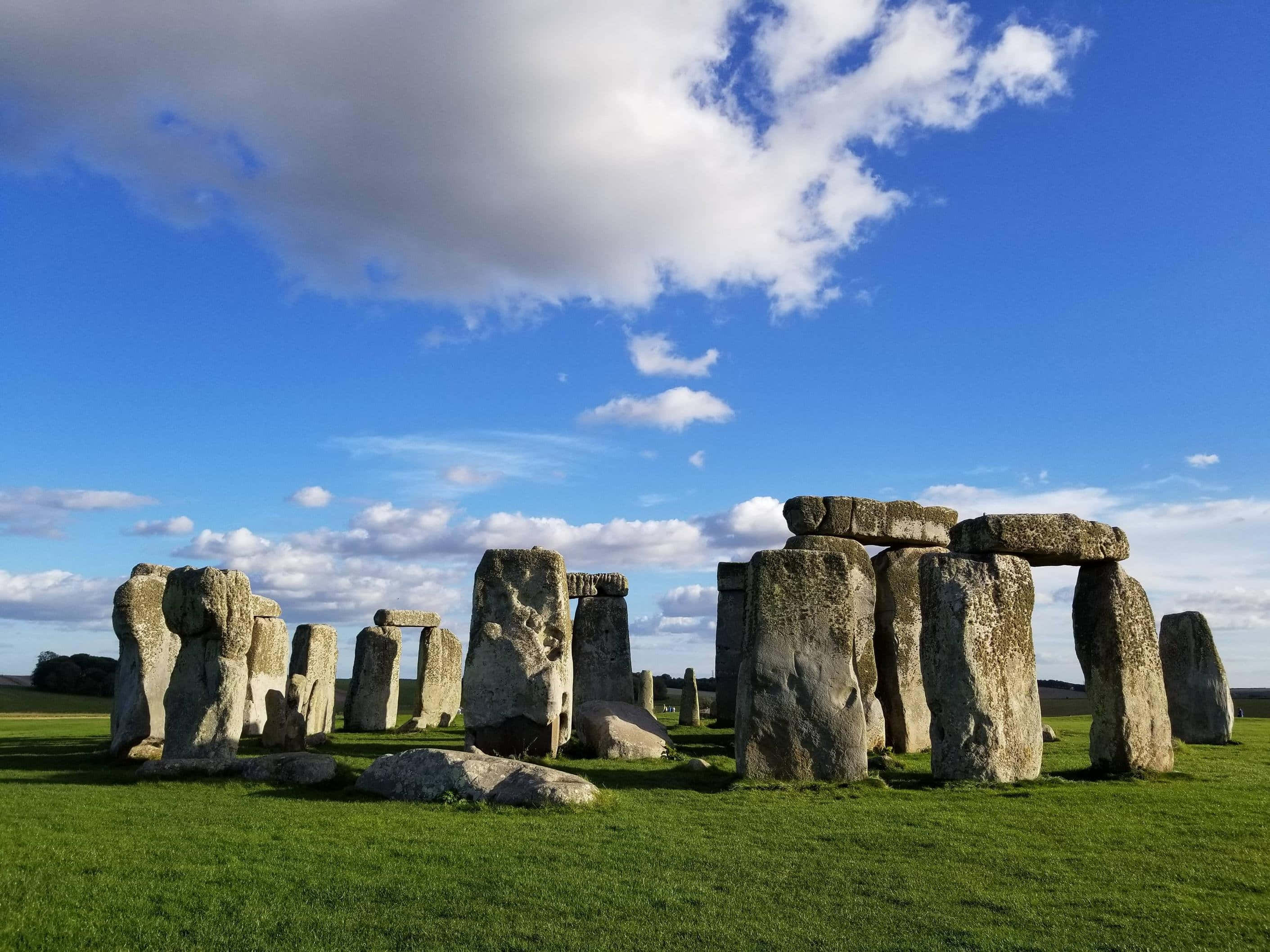 England 桌布 壁紙 — 巨石陣的古老立石從鮮綠色的草地上雄偉地升起，在點綴著蓬鬆白雲的明亮藍天下。