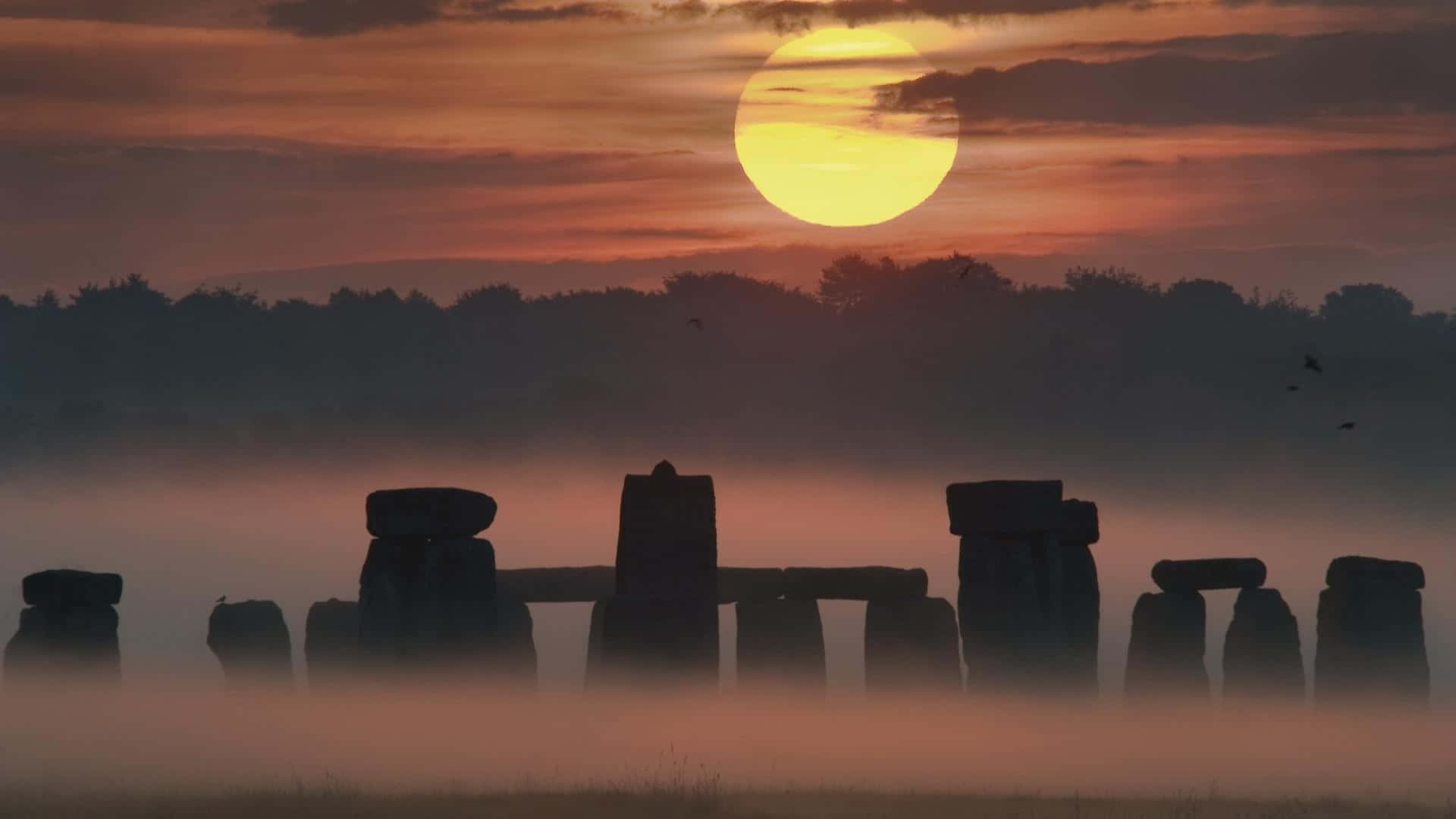 England 桌布 壁紙 — 巨石陣的霧濛濛黎明，一輪巨大的太陽從古老的立石後升起，投下長長的影子。