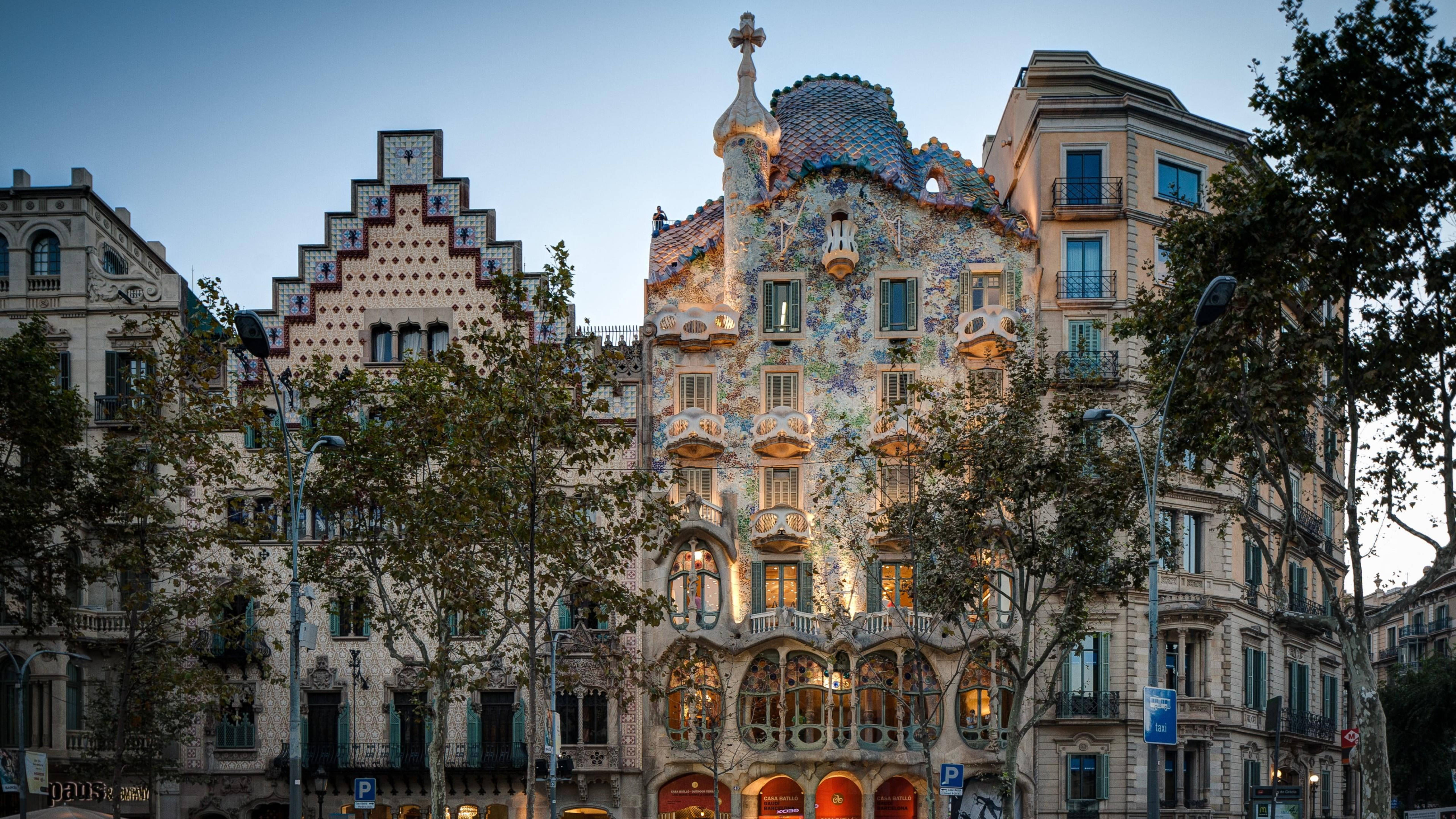 西班牙 桌布 壁紙 — 巴塞隆納 Casa Batlló 的迷人黃昏景色，其馬賽克外牆在柔和藍天下溫暖地發光。