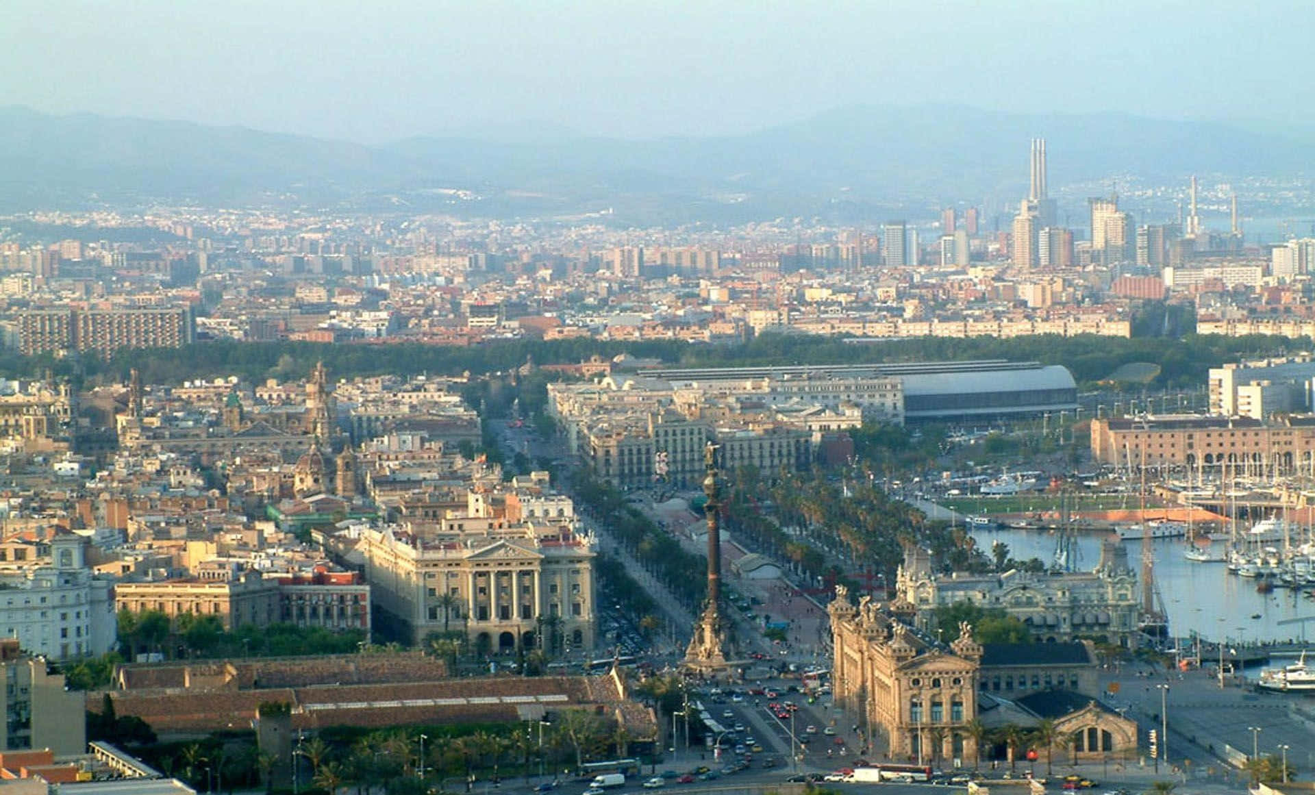 Barcelona 桌布 壁紙 — 巴塞隆納城市景觀的全景視圖，包括歷史建築、停滿船隻的港口，以及在朦朧天空下的遠山。