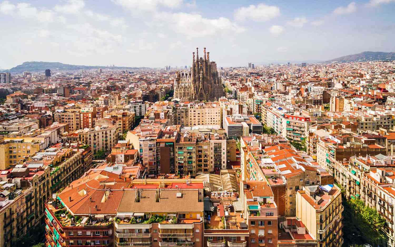 Barcelona 桌布 壁紙 — 巴塞隆納密集城市擴張的鳥瞰圖，聖家堂在明亮的藍天下聳立於陶土屋頂之上。