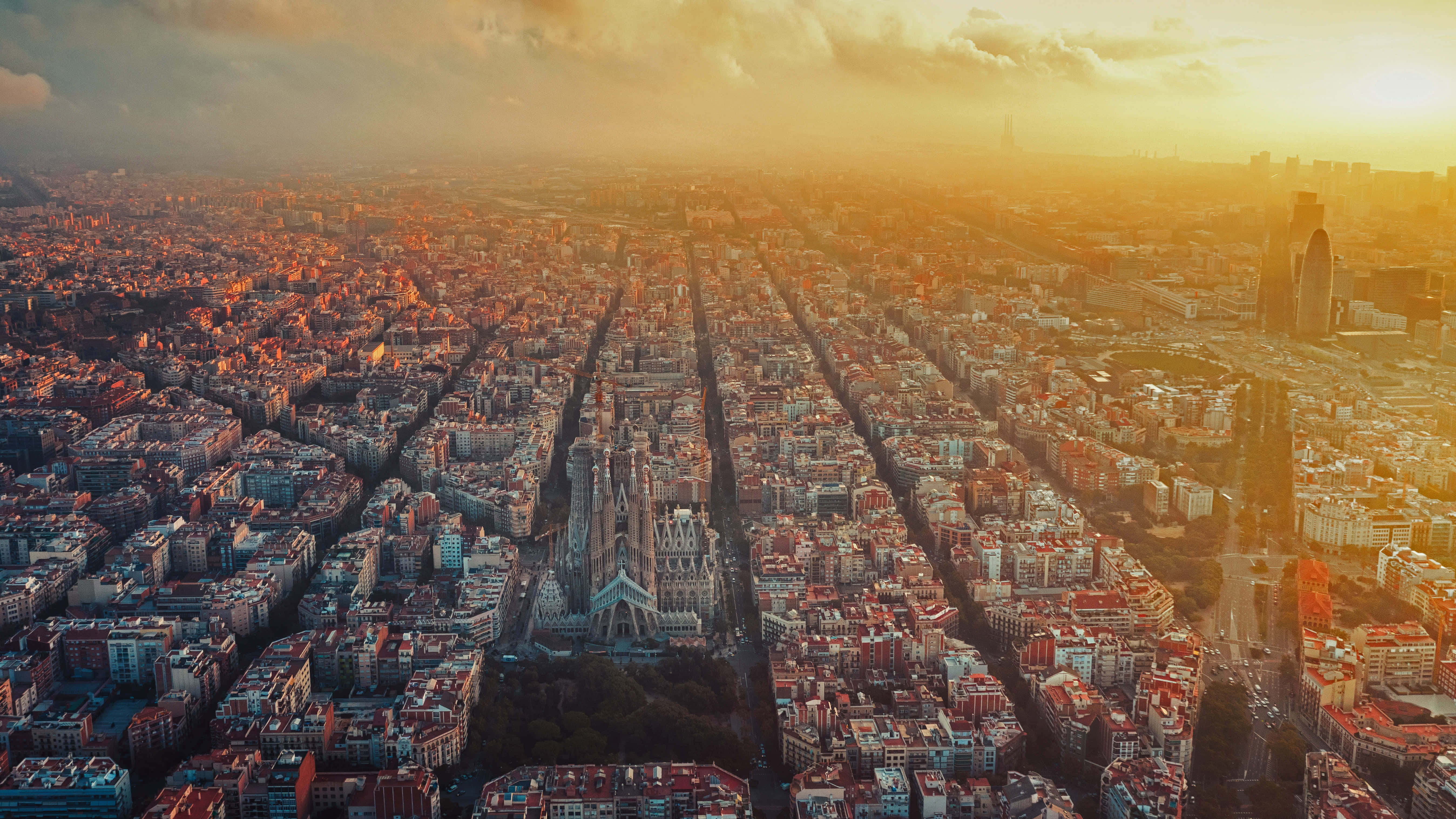 Spanish 桌布 壁紙 — 巴塞隆納黃金時段的鳥瞰圖，聖家堂在溫暖的陽光下閃耀。