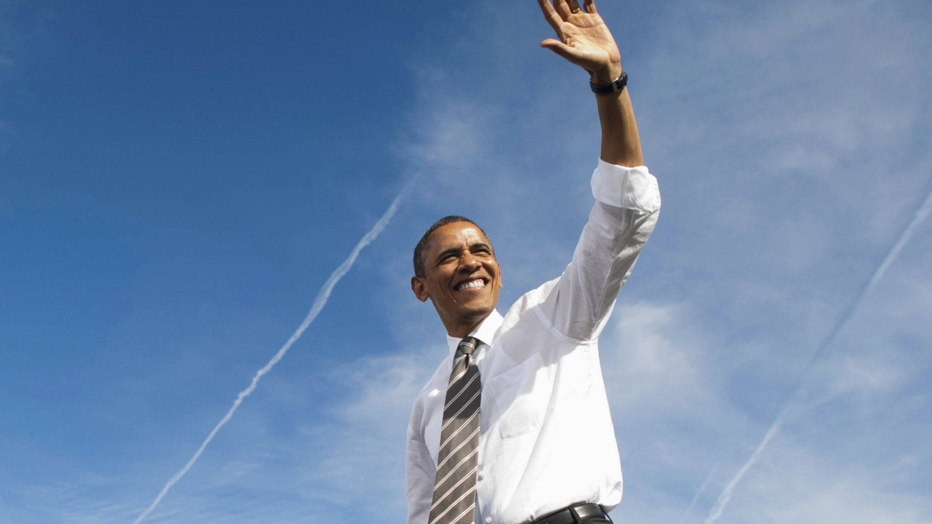 Barack 桌布 壁紙 — 巴拉克·歐巴馬在帶有飛機軌跡的明亮藍天下愉快地揮手。