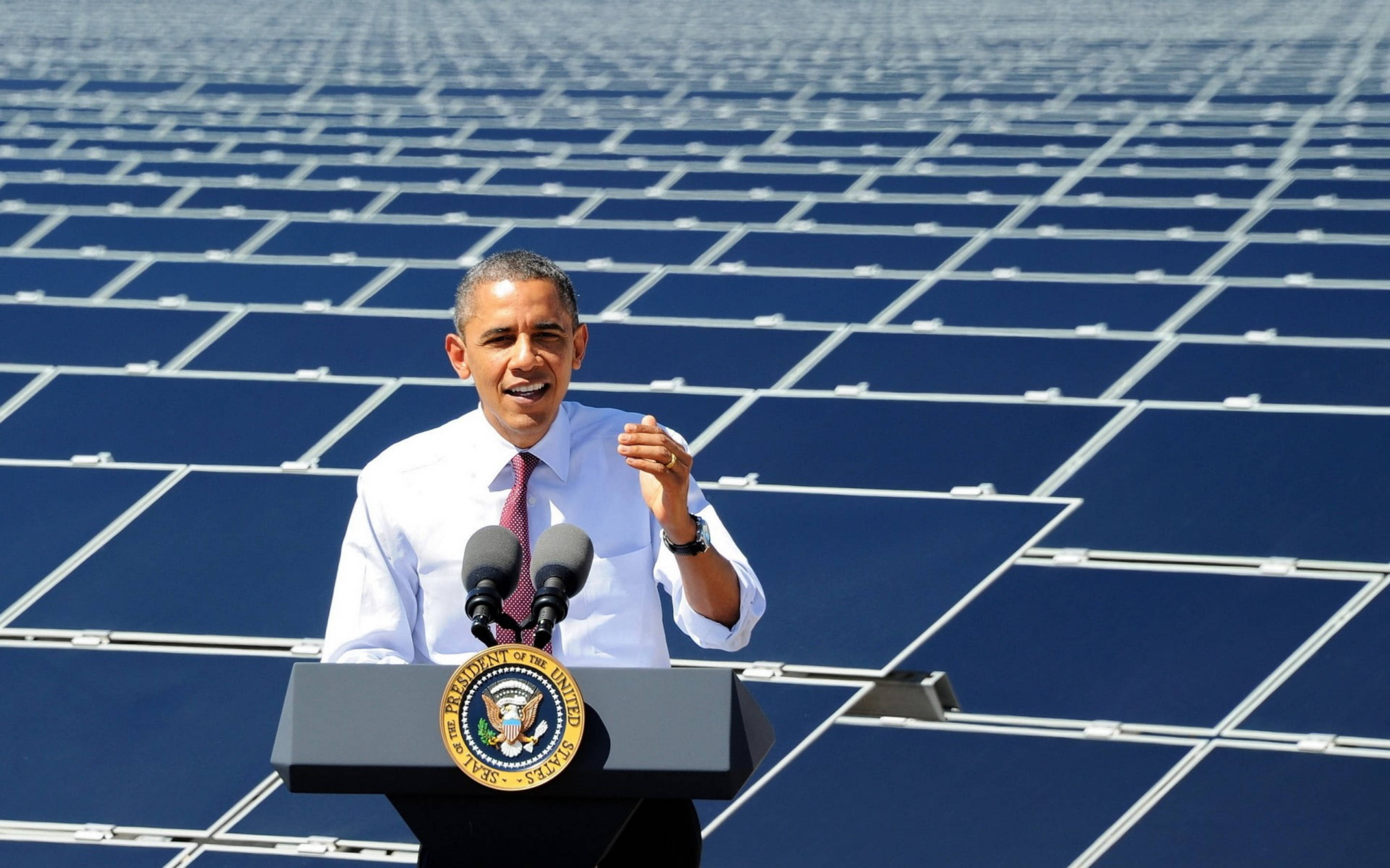 Barack 桌布 壁紙 — 巴拉克·歐巴馬在總統印章的講台上，在明亮的日光下，以廣闊的藍色太陽能電池板為背景發表演講。