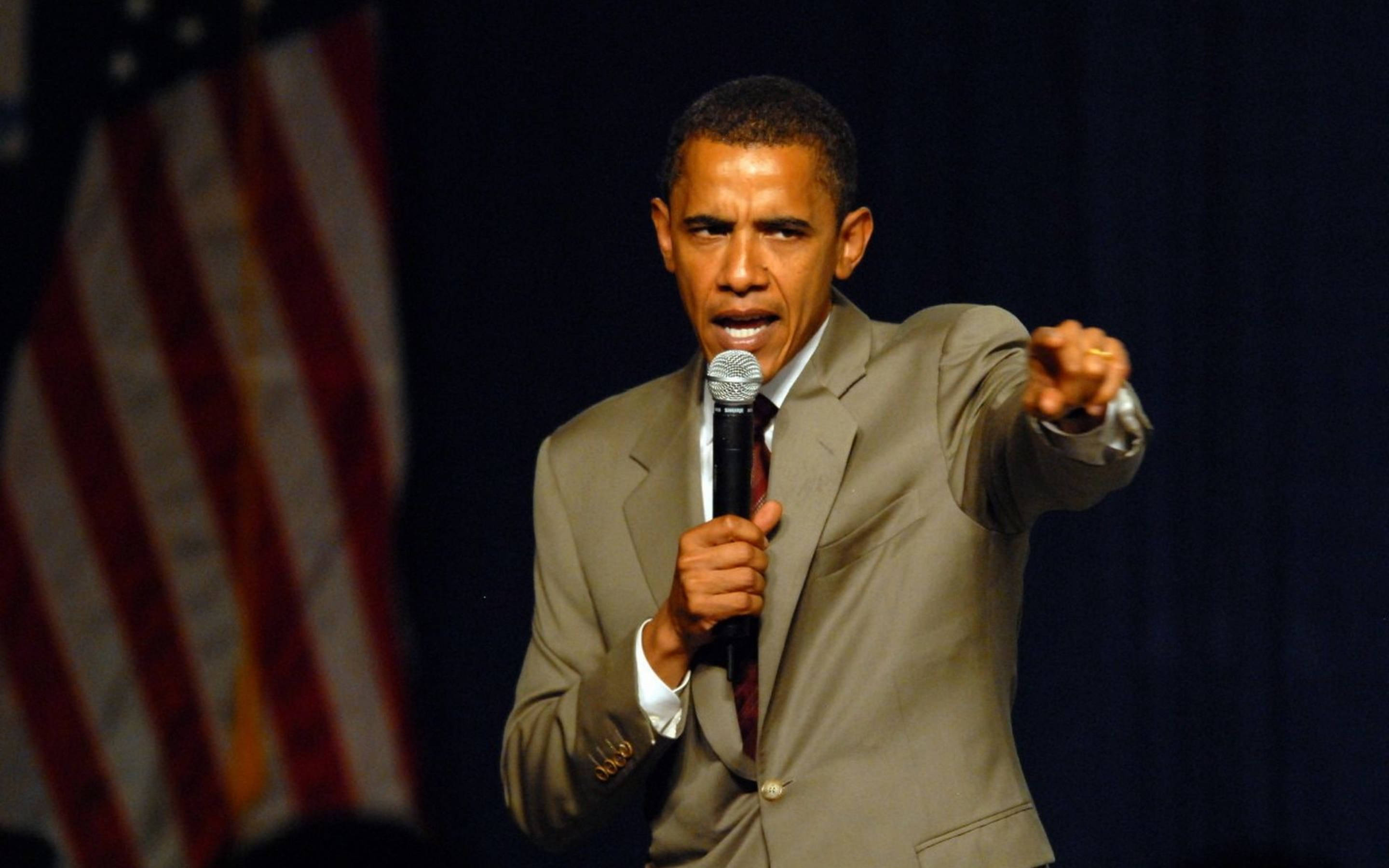 Barack 桌布 壁紙 — 巴拉克·歐巴馬熱情地對著麥克風說話，同時向前指，背景有模糊的美國國旗。