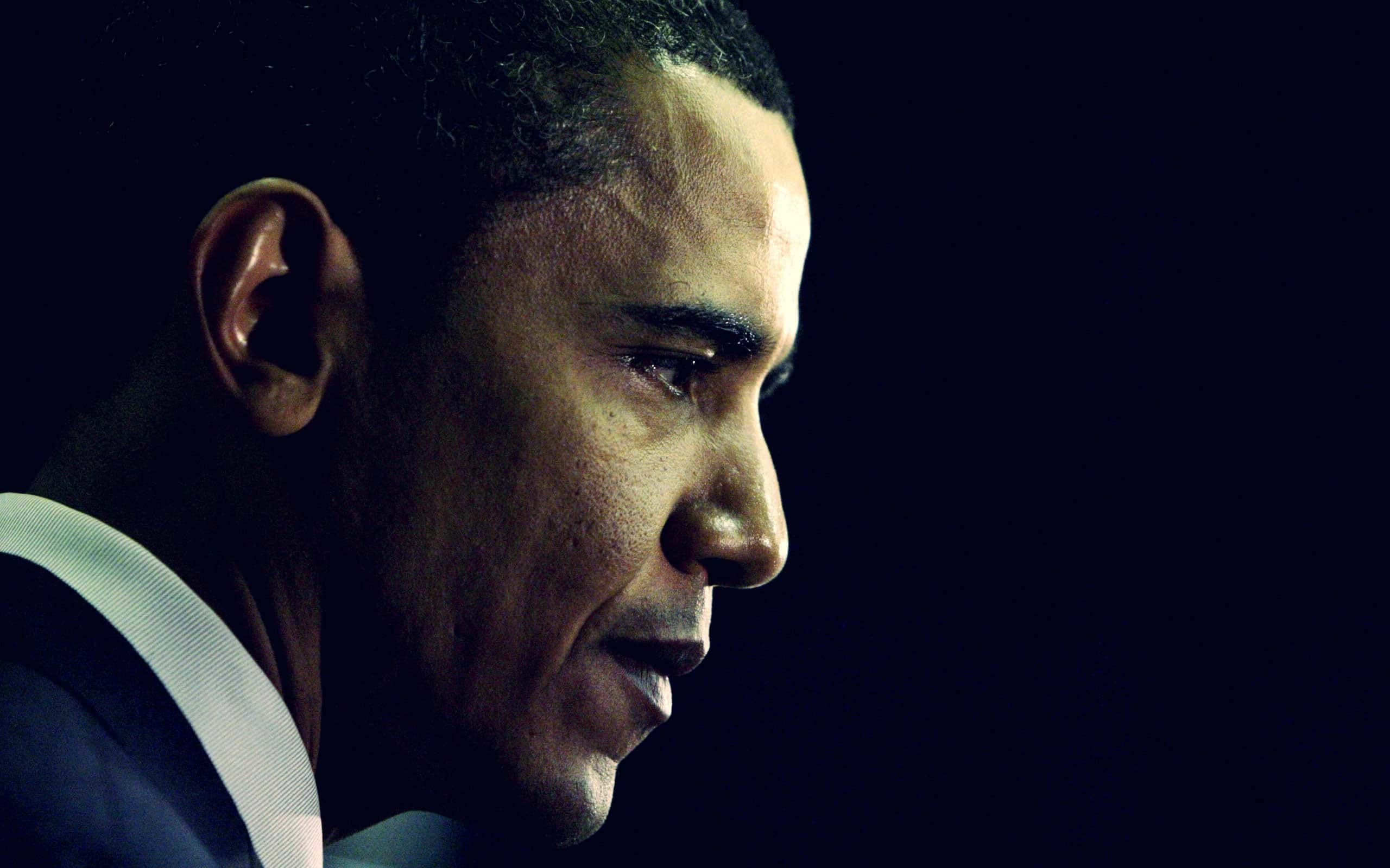 Barack Obama 桌布 壁紙 — 巴拉克·歐巴馬的側面特寫肖像，背景為深色，戲劇性的燈光突出其面部特徵。