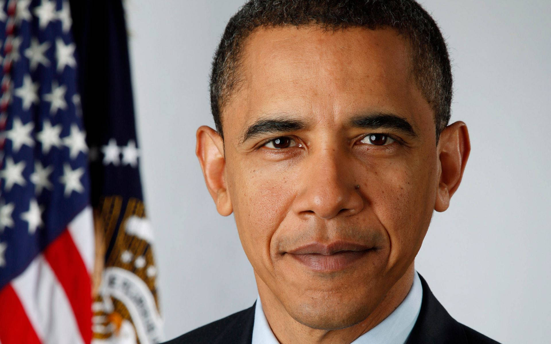 Barack 桌布 壁紙 — 巴拉克·歐巴馬的近距離肖像，身穿深色西裝，身後有美國國旗和總統印章。