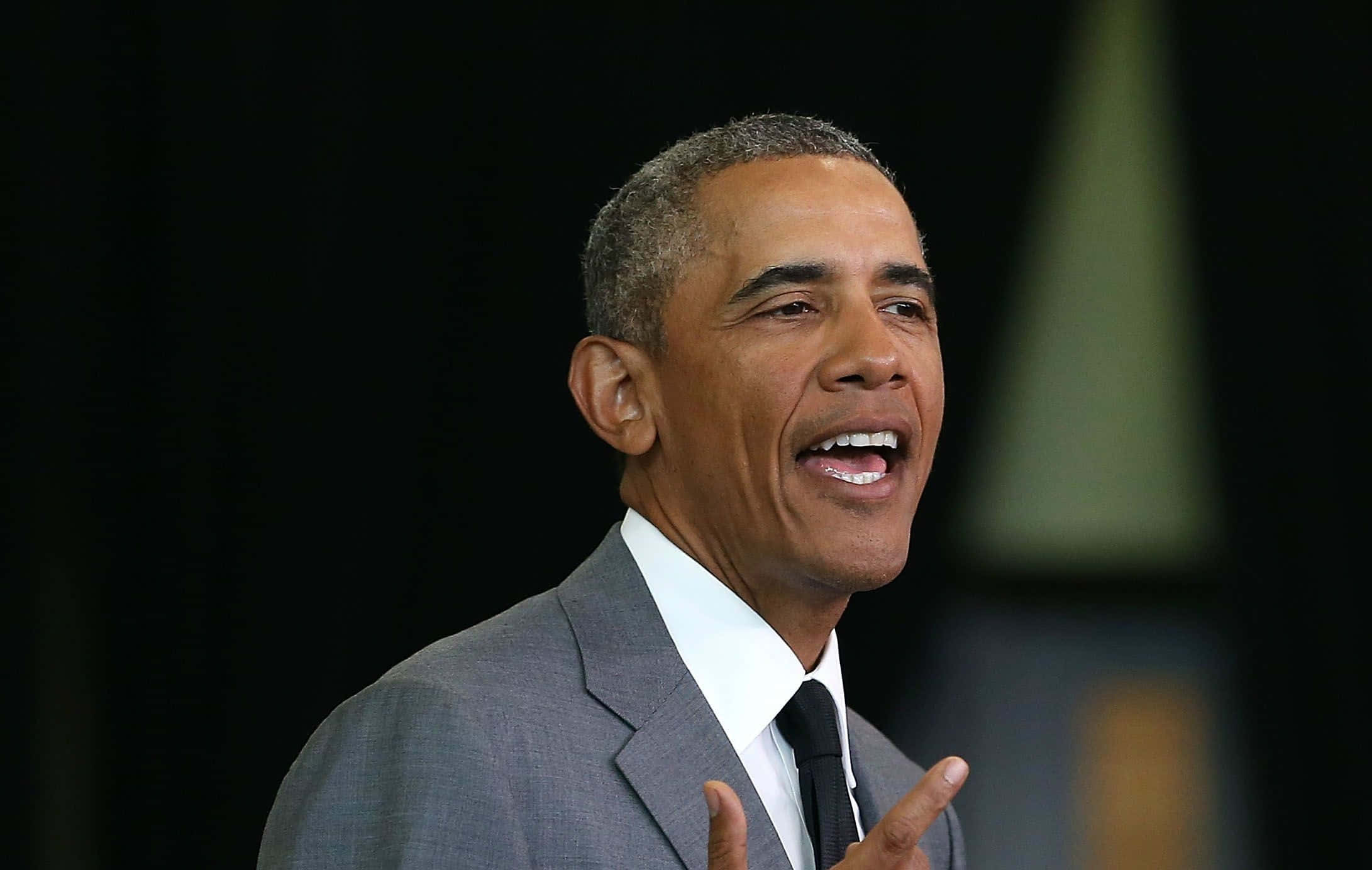Barack Obama 桌布 壁紙 — 巴拉克·歐巴馬穿著灰色西裝，在深色背景前雙手比劃，燦爛地微笑。