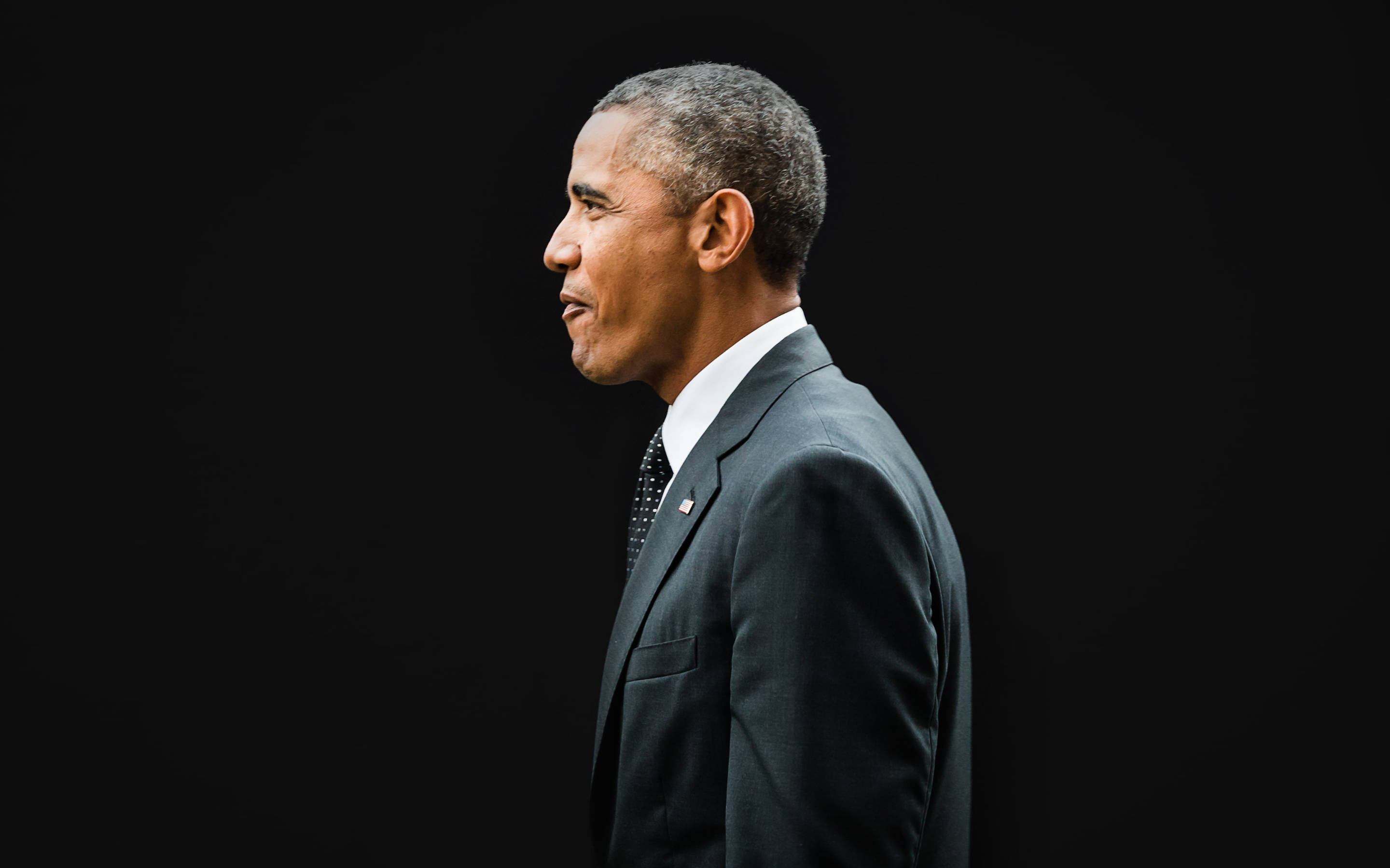 Barack 桌布 壁紙 — 巴拉克·歐巴馬穿著鋒利的西裝，在聚焦燈光下以側面輪廓站在純黑背景前。