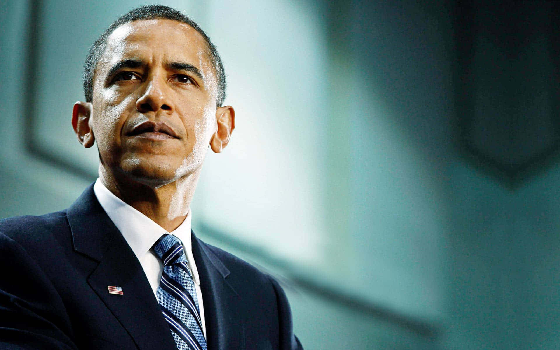 Barack Obama 桌布 壁紙 — 巴拉克·歐巴馬身穿深色西裝和條紋領帶，在模糊的藍綠色背景下，表情嚴肅地向上凝視。