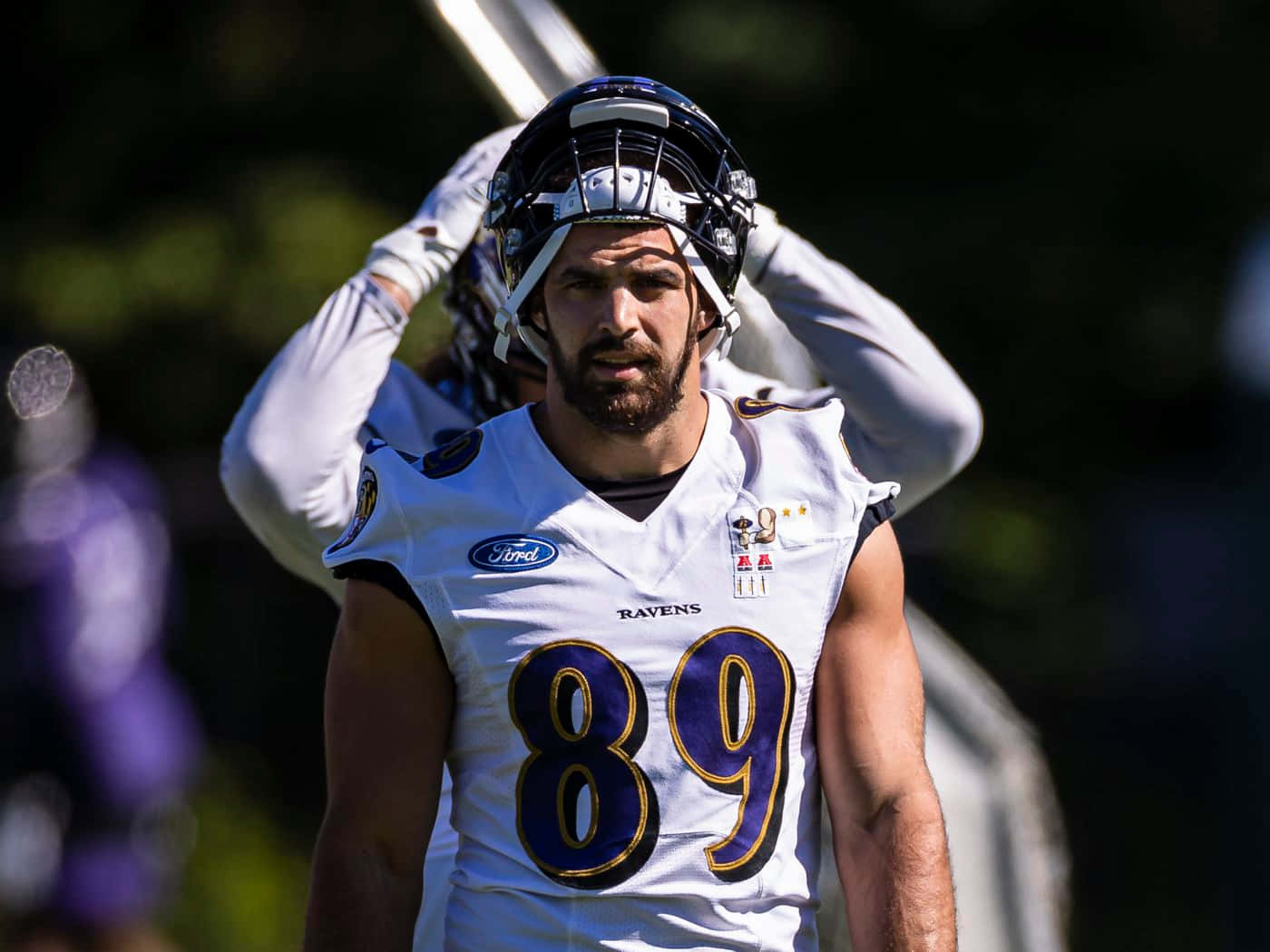Mark Andrews 桌布 壁紙 — 巴爾的摩烏鴉隊美式足球員身穿白色89號球衣，在球場明亮的陽光下調整頭盔。