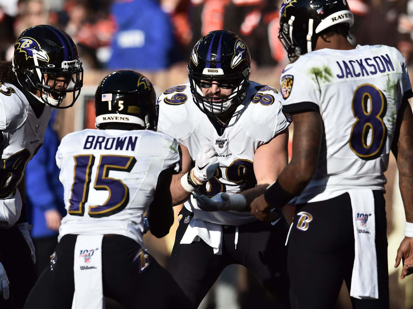 NFL Teams 桌布 壁紙 — 巴爾的摩烏鴉隊美式足球員身穿白色和紫色球衣，在比賽期間於球場上激烈地圍成一圈。