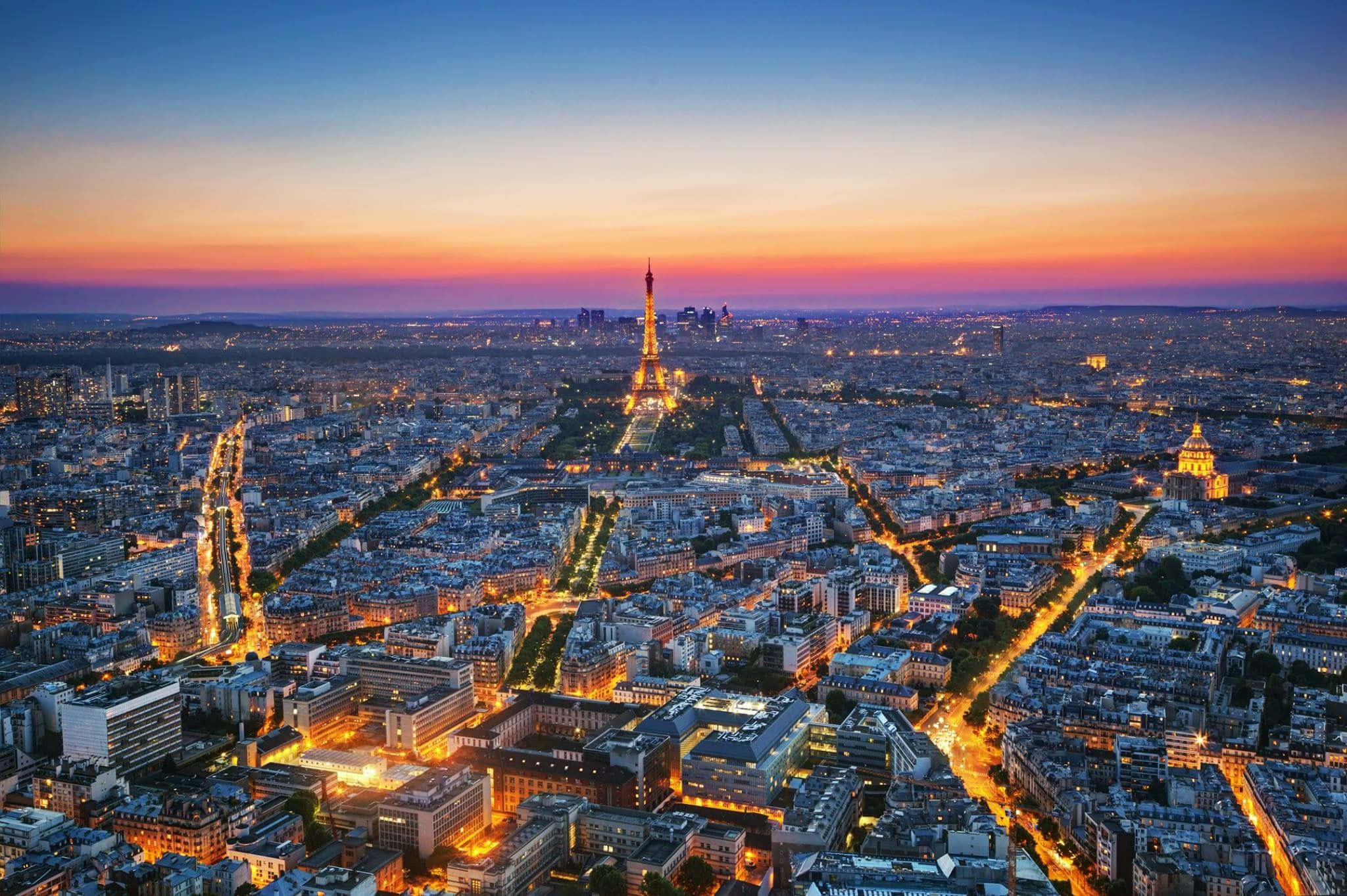 France 桌布 壁紙 — 巴黎天際線在暮色中，艾菲爾鐵塔在橙色和藍色的漸變天空中閃耀。