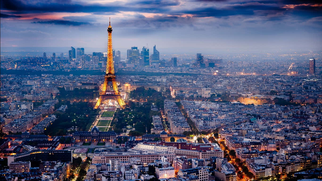 Eiffel Tower 桌布 壁紙 — 巴黎天際線在黃昏時分，艾菲爾鐵塔在紫色和橙色的雲層天空中閃耀著金色光芒。