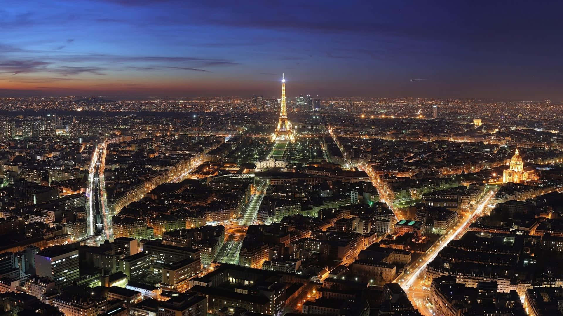 Paris Desktop 桌布 壁紙 — 巴黎天際線在黃昏時分，艾菲爾鐵塔在燈火通明的街道和建築物上方閃耀。