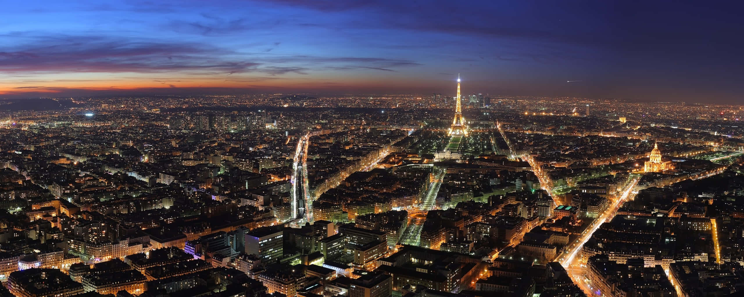 Paris At Night 桌布 壁紙 — 巴黎天際線在黃昏時分，艾菲爾鐵塔在深藍色和橙色的漸變天空中閃耀。