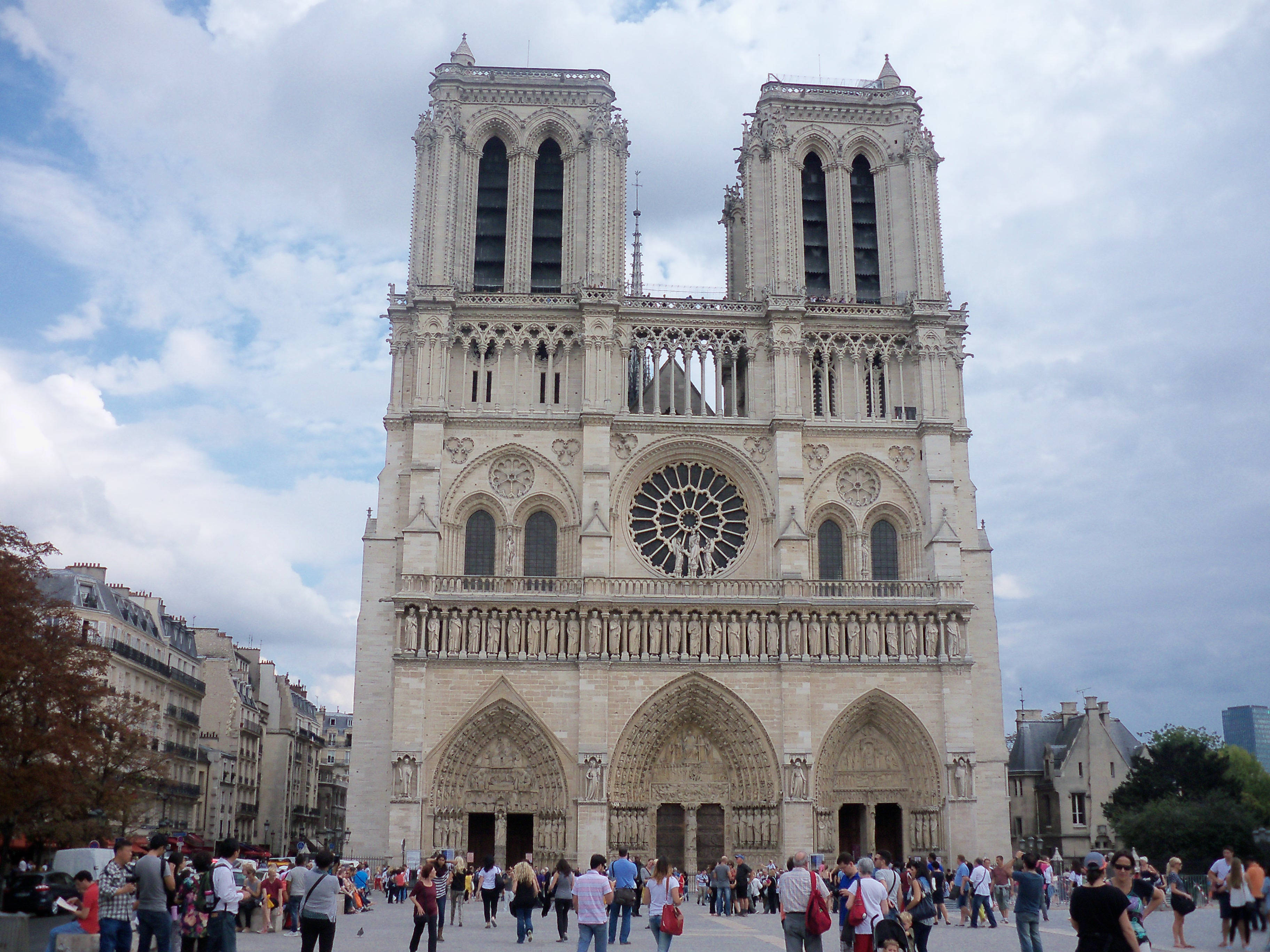 Notre Dame 桌布 壁紙 — 巴黎宏偉的哥德式聖母院大教堂在陰天高聳矗立，人群聚集在其腳下。