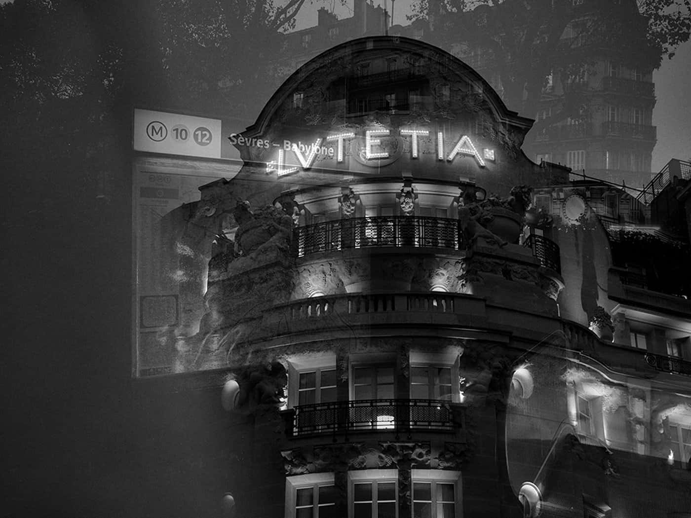 Haunted Hotels 桌布 壁紙 — 巴黎建築物的黑白夜間倒影，帶有 'TETIA' 霓虹燈招牌和地鐵站疊加效果。