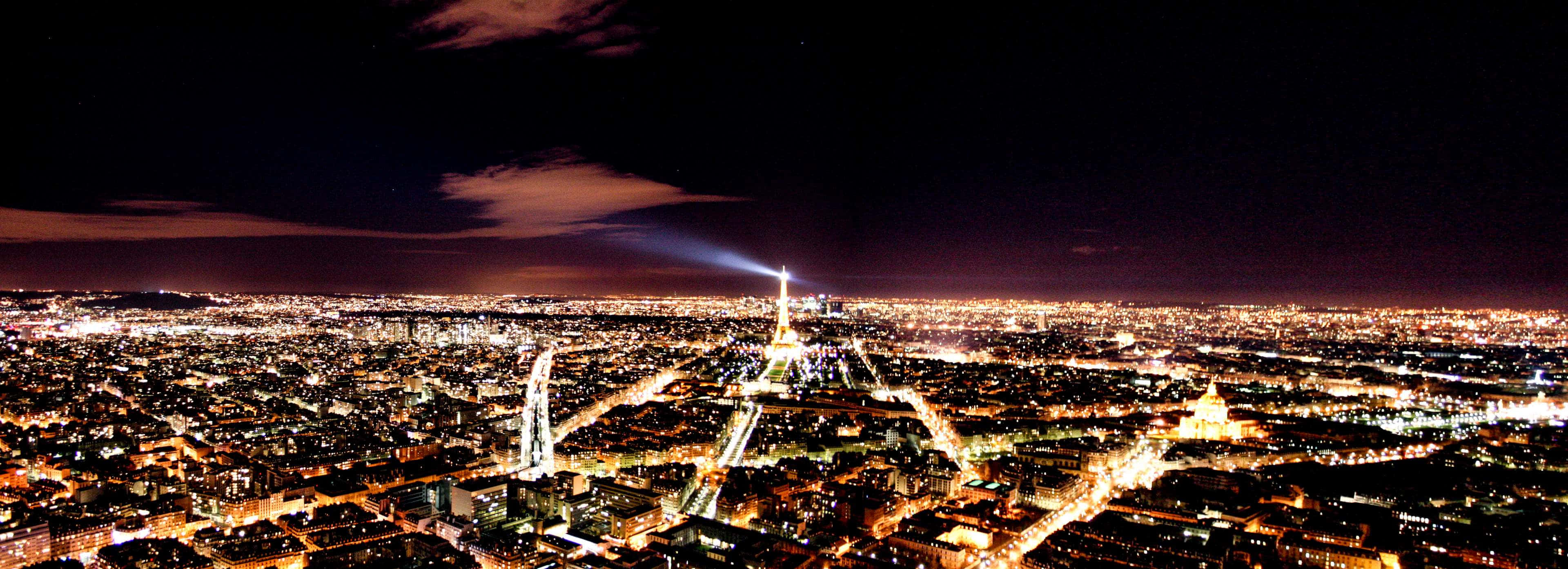 Paris At Night 桌布 壁紙 — 巴黎的夜間空中景觀，展示在黑暗天空下被照亮的艾菲爾鐵塔和蔓延的城市燈光。
