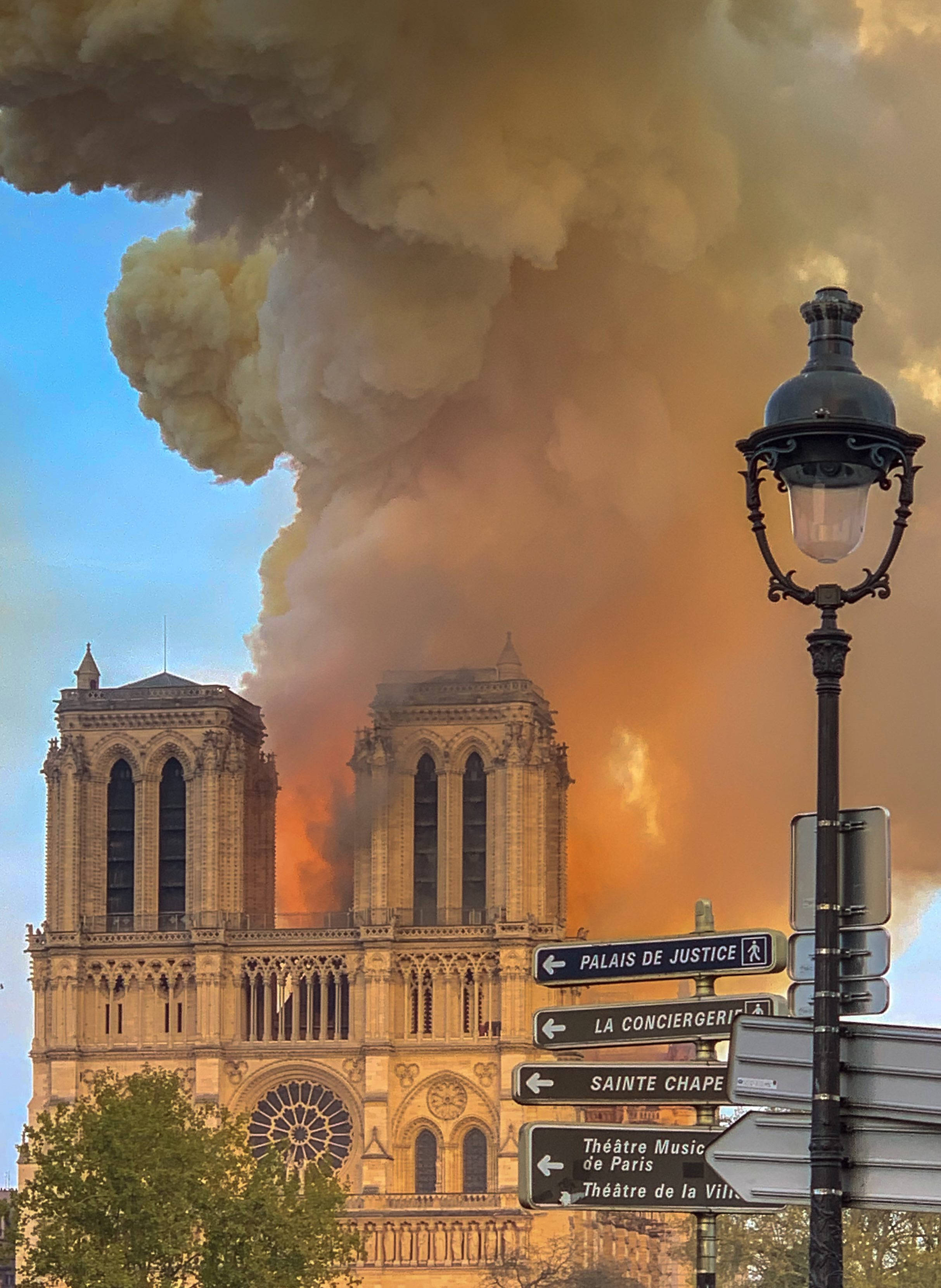 Notre Dame 桌布 壁紙 — 巴黎聖母院冒出濃煙，火焰在其標誌性雙塔後方升起，藍天之下。