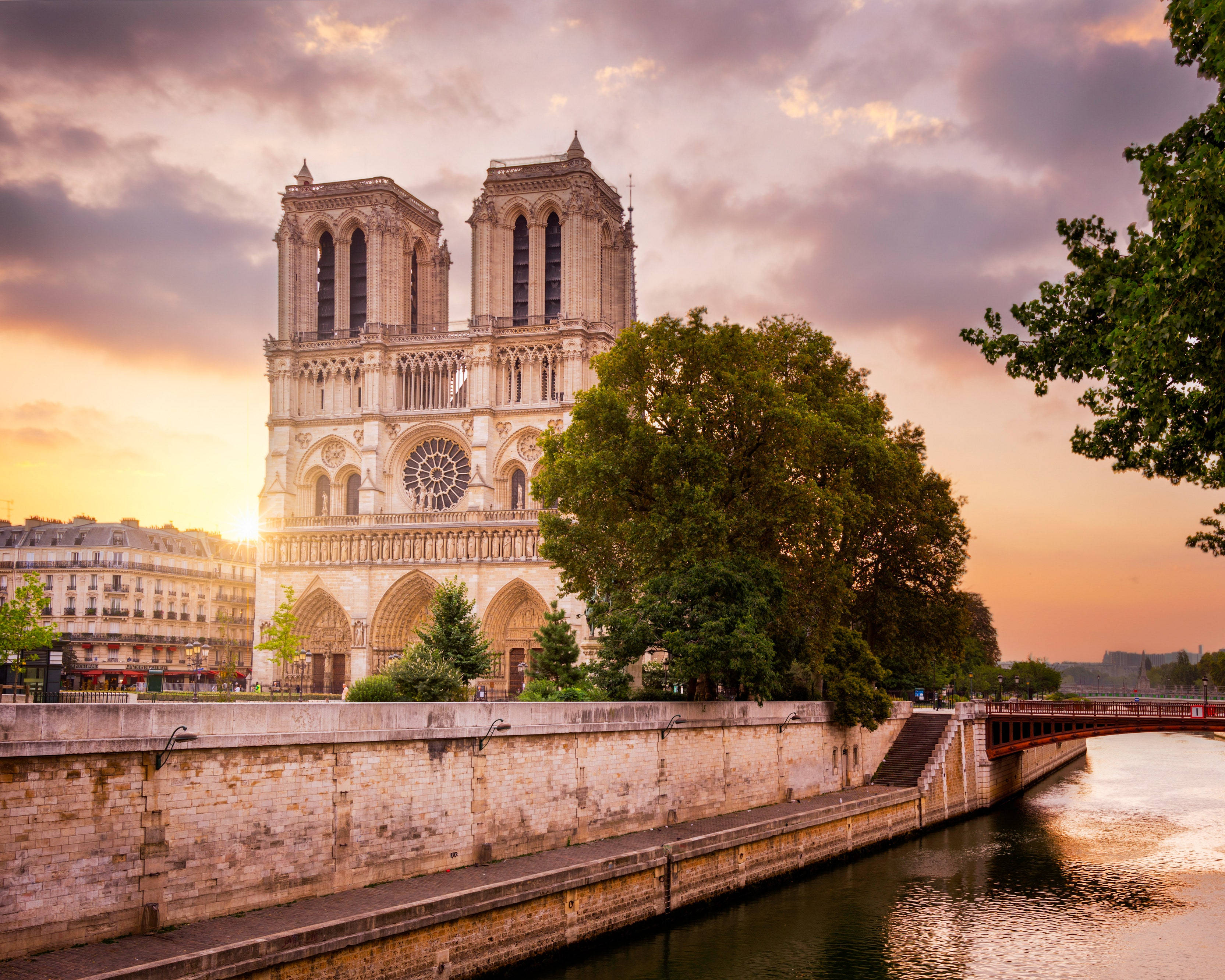 Notre Dame 桌布 壁紙 — 巴黎聖母院在日落時分雄偉矗立，溫暖的金色光芒照亮其哥德式建築，並在塞納河上反射。
