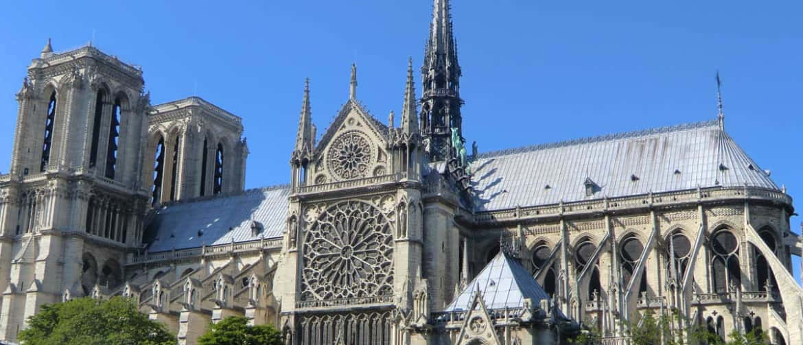 Gothic Architecture 桌布 壁紙 — 巴黎聖母院在晴朗的藍天下巍然聳立，擁有複雜的哥德式建築和突出的玫瑰窗。