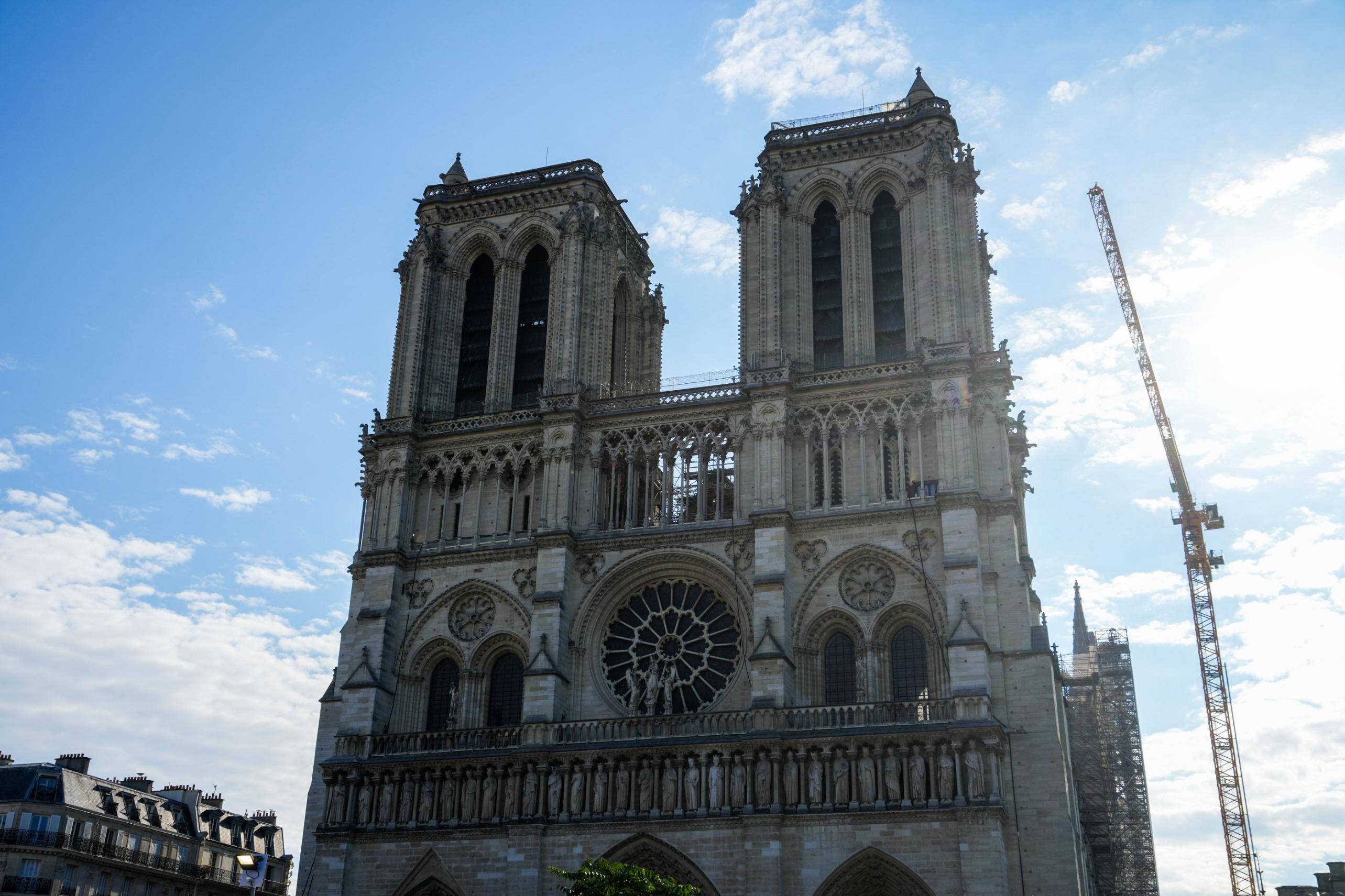 Notre Dame 桌布 壁紙 — 巴黎聖母院在晴朗藍天和零星白雲下巍峨矗立，旁邊可見一座建築起重機。