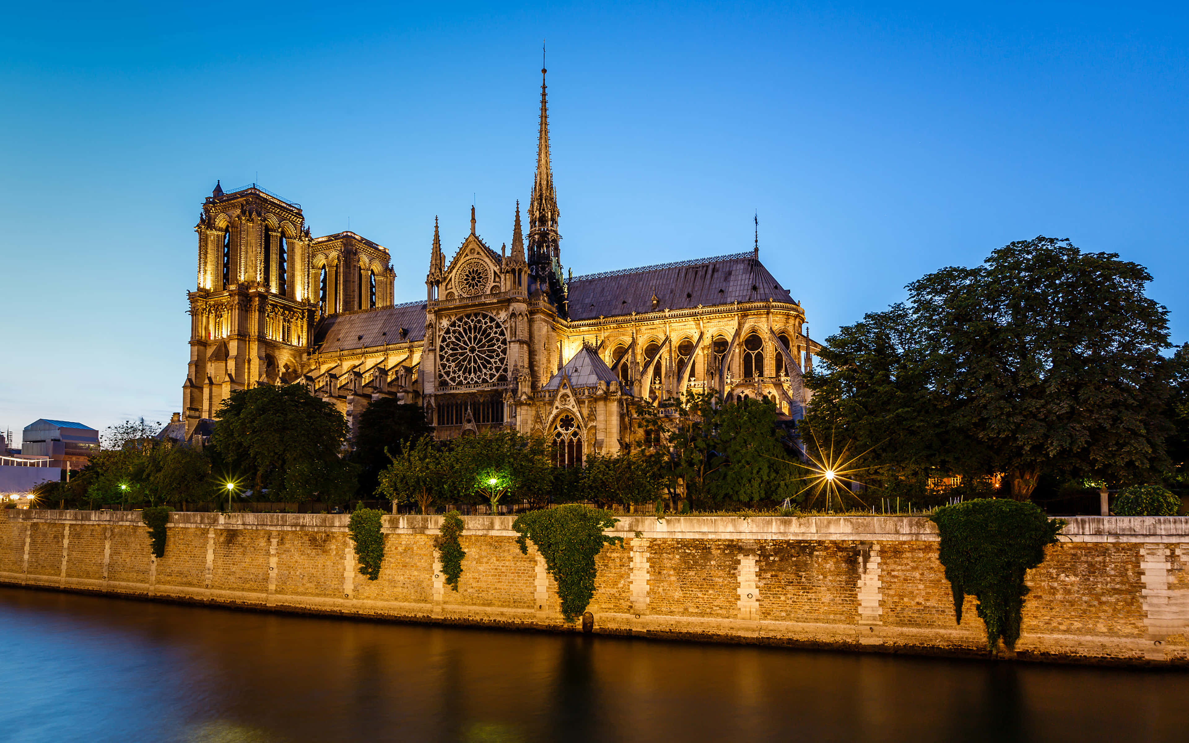 Notre Dame 桌布 壁紙 — 巴黎聖母院在暮色天空下溫暖地發光，倒映在平靜的塞納河水中。