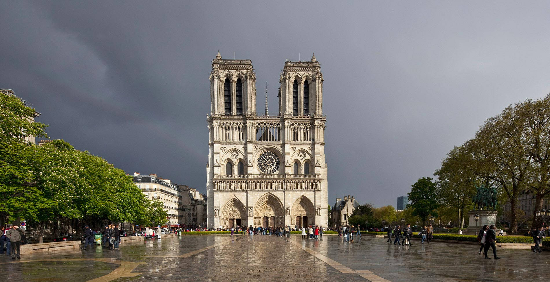 Notre Dame 桌布 壁紙 — 巴黎聖母院在陰沉的暴風雨天空下巍然聳立，濕漉漉的鵝卵石映照出其哥德式輪廓。
