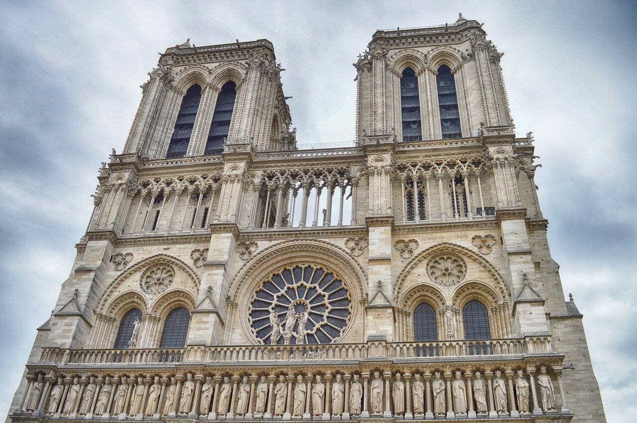 Notre Dame 桌布 壁紙 — 巴黎聖母院宏偉的哥德式正面，雙塔、玫瑰窗和雕像，天空多雲。