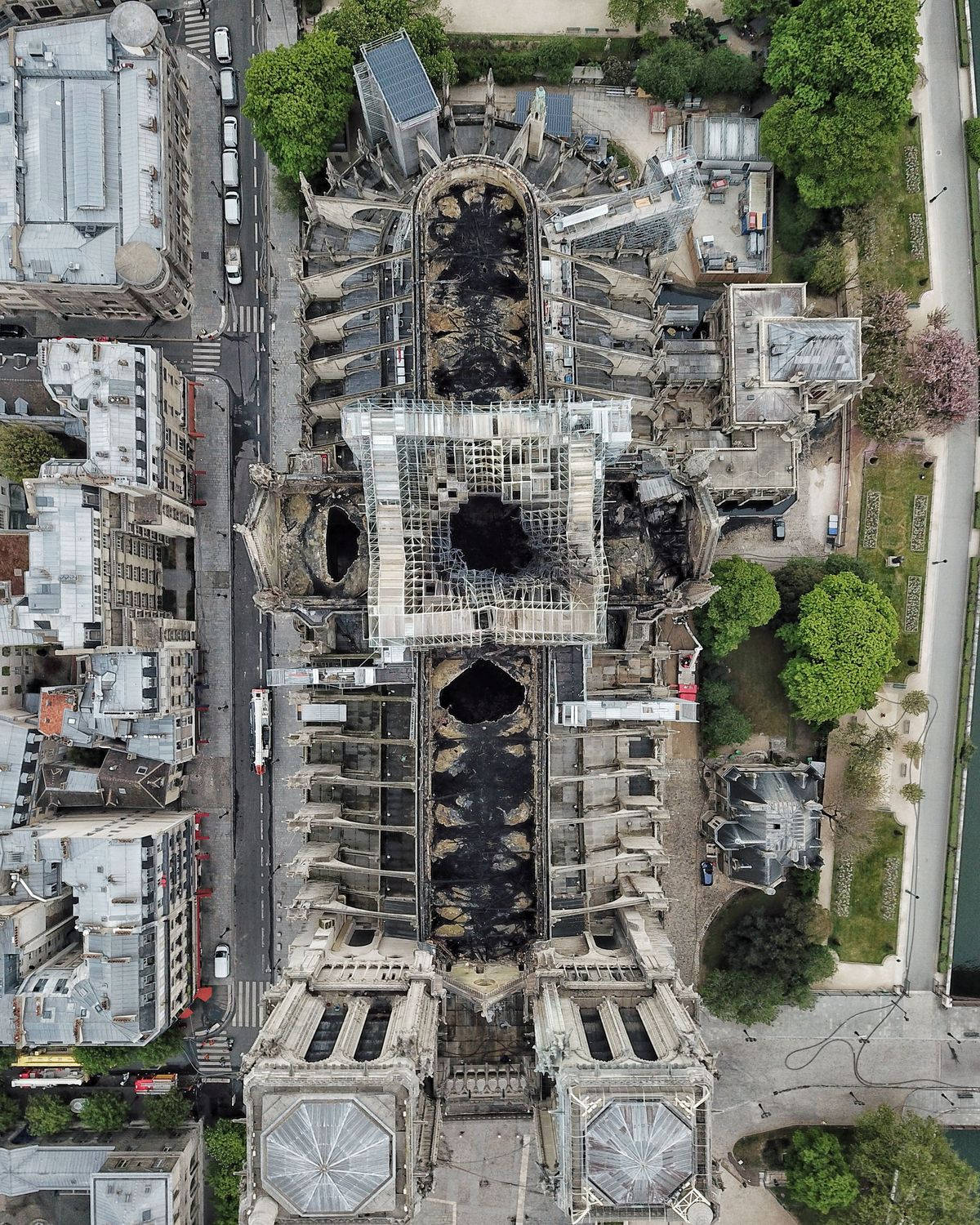 Notre Dame 桌布 壁紙 — 巴黎聖母院的鳥瞰圖，顯示其屋頂和尖塔在周圍城市建築中遭受大面積火災損壞。