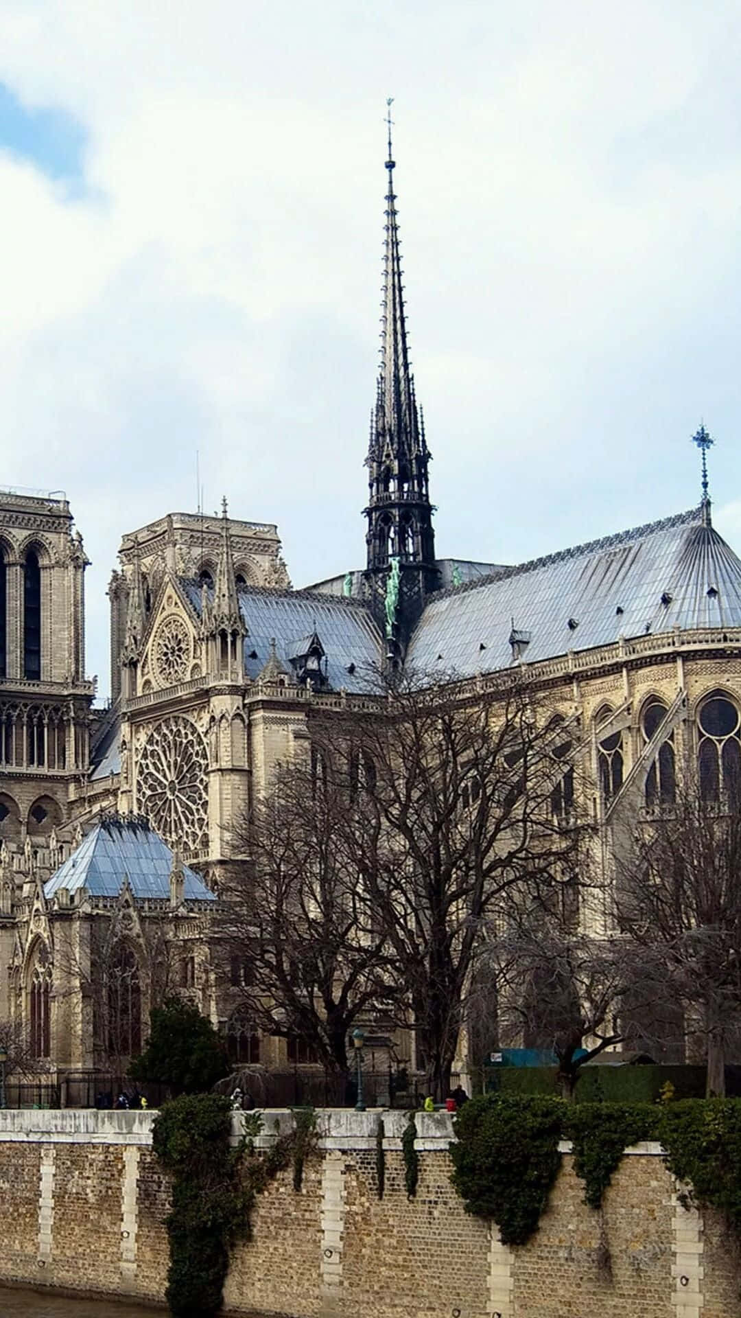 Notre Dame 桌布 壁紙 — 巴黎聖母院高聳入雲，其標誌性尖塔和玫瑰窗在陰雲密布的天空下巍然屹立。