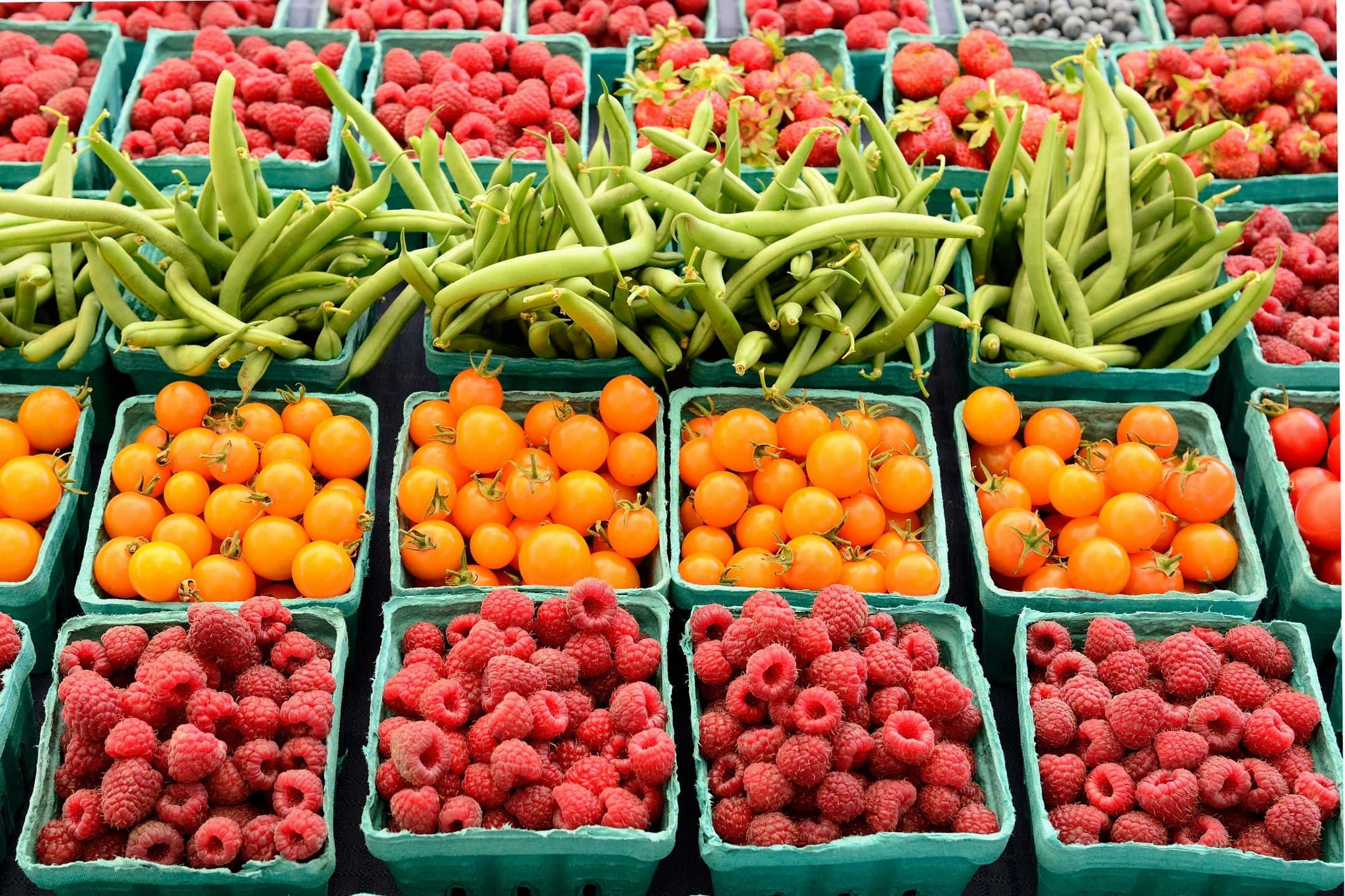 Farmers Market 桌布 壁紙 — 市場中綠色板條箱內新鮮農產品的鮮豔展示，包括青豆、橙色櫻桃番茄和紅覆盆子。