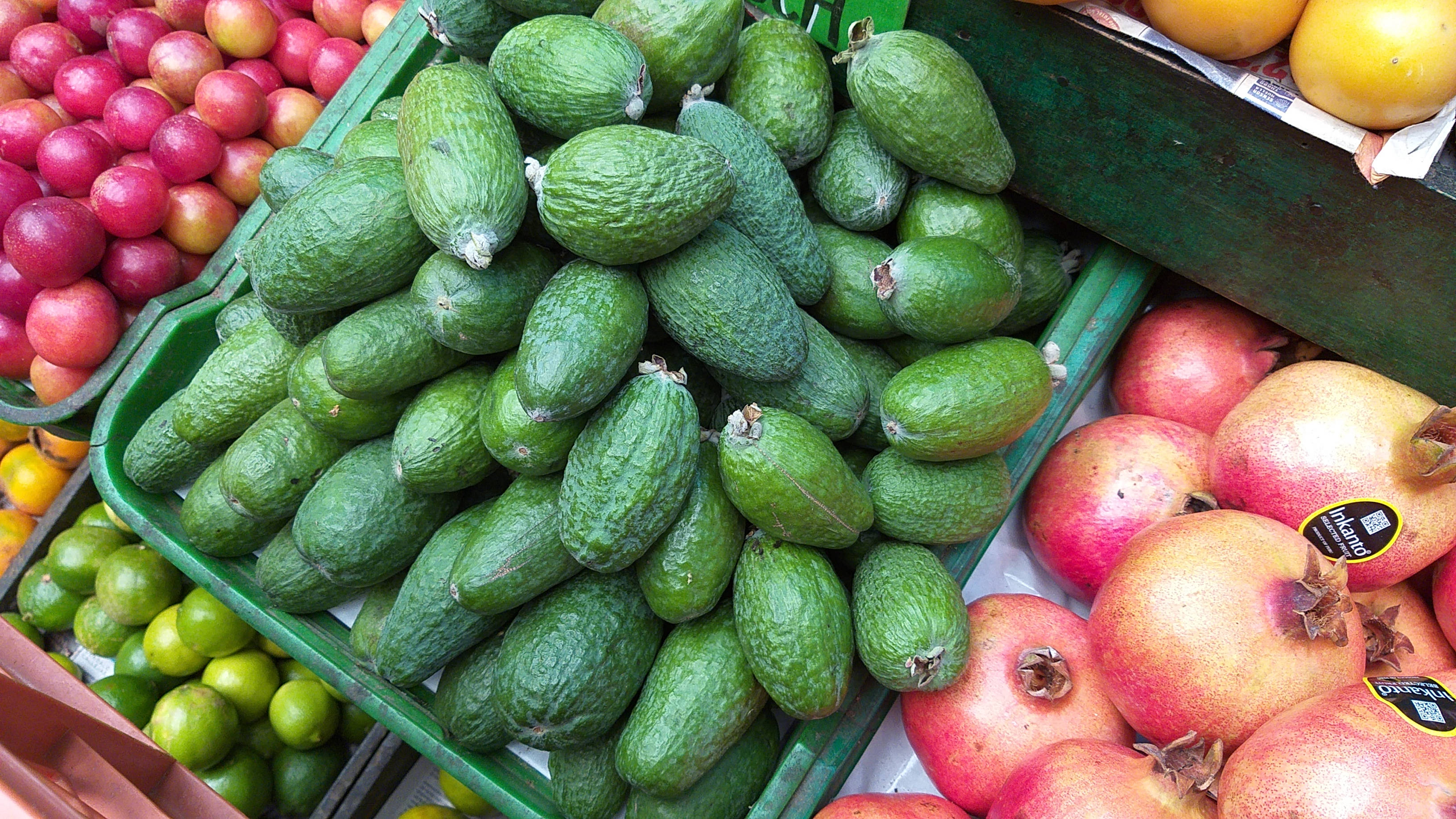 Fruit 桌布 壁紙 — 市場攤位上綠色木箱中，新鮮綠色菲油果與紅蘋果、石榴和青檸的鮮豔展示。