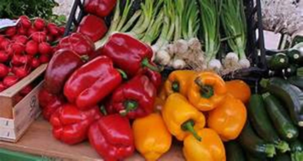 Fruit 桌布 壁紙 — 市場攤位上陳列著色彩繽紛的新鮮農產品，包括紅甜椒、黃甜椒、小蘿蔔、大蒜和櫛瓜。