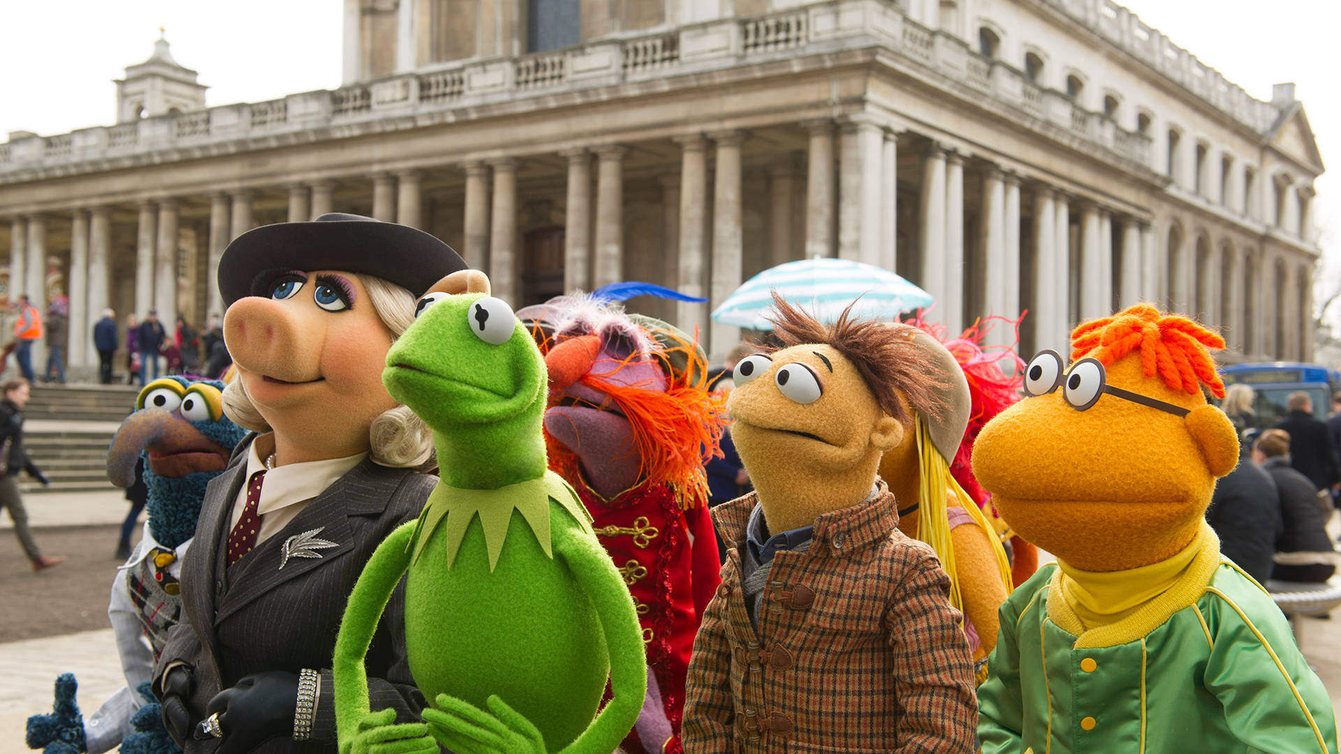 muppets 桌布 壁紙 — 布偶角色們穿著戲服，在有柱子的宏偉古典建築前愉快地擺姿勢。