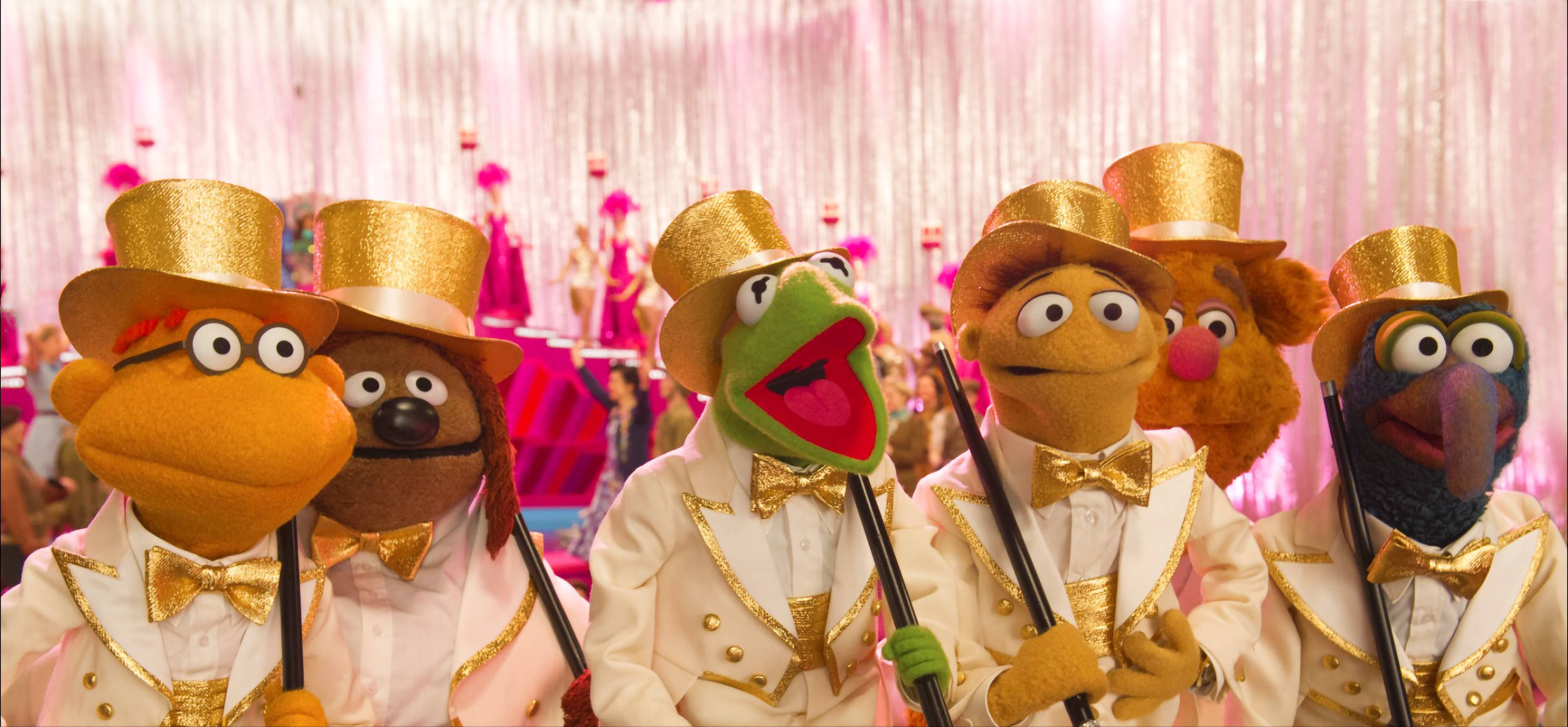 muppets 桌布 壁紙 — 布偶角色穿著金色邊飾的燕尾服和高帽，在閃閃發光的粉紅色舞台上表演，背景閃爍。