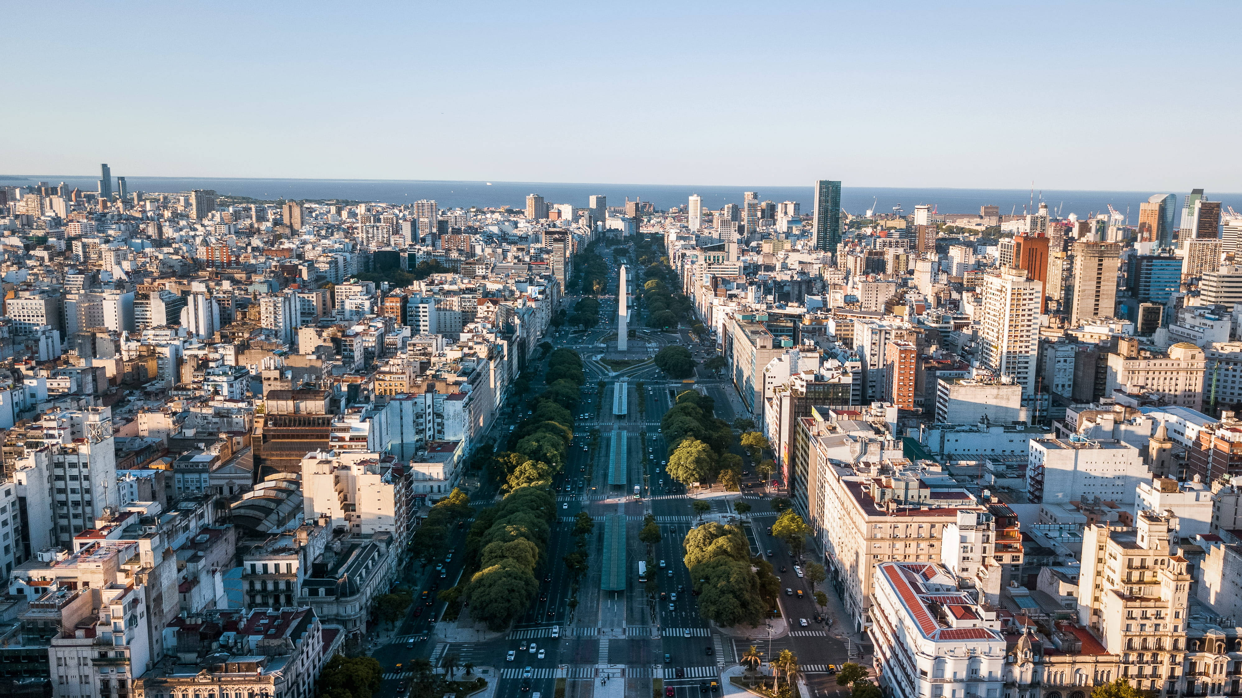Argentina 桌布 壁紙 — 布宜諾斯艾利斯寬闊大道的鳥瞰圖，兩旁樹木和建築物林立，遠處是海洋地平線。