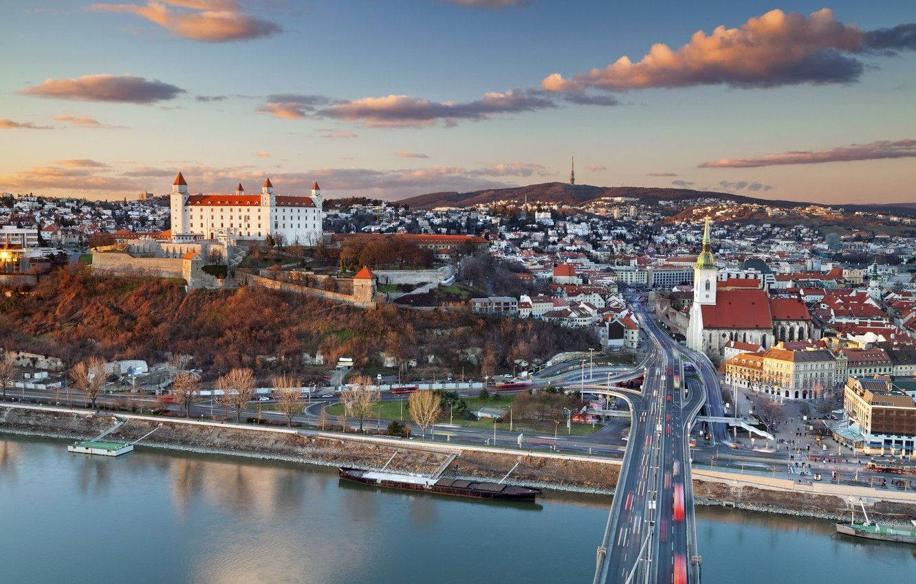 Slovakia 桌布 壁紙 — 布拉迪斯拉發城堡的空中日落景觀，坐落在俯瞰多瑙河和城市景觀的山丘上，有一座繁忙的橋樑。