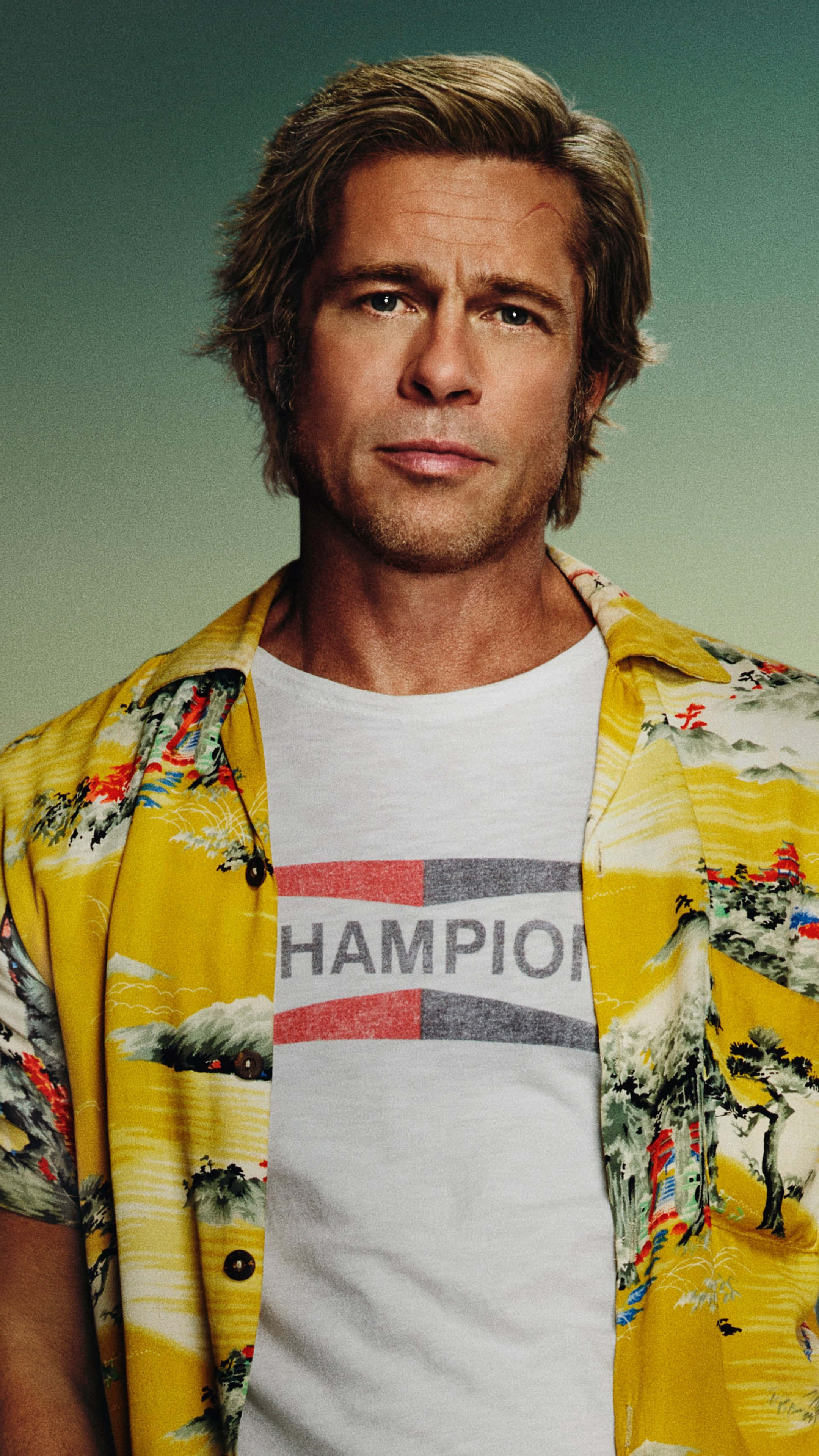 Brad Pitt 桌布 壁紙 — 布萊德彼特穿著一件鮮黃色夏威夷襯衫，上面有山脈圖案，內搭白色Champion T恤，背景是柔和的藍綠色。