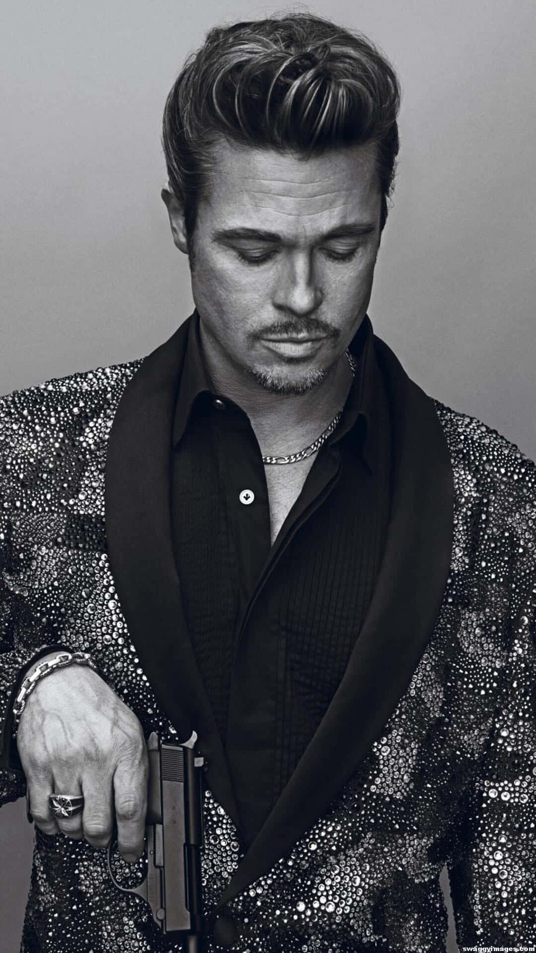 Brad Pitt 桌布 壁紙 — 布萊德彼特身穿閃亮銀色外套，手持槍枝，表情嚴肅，在單色工作室肖像中。